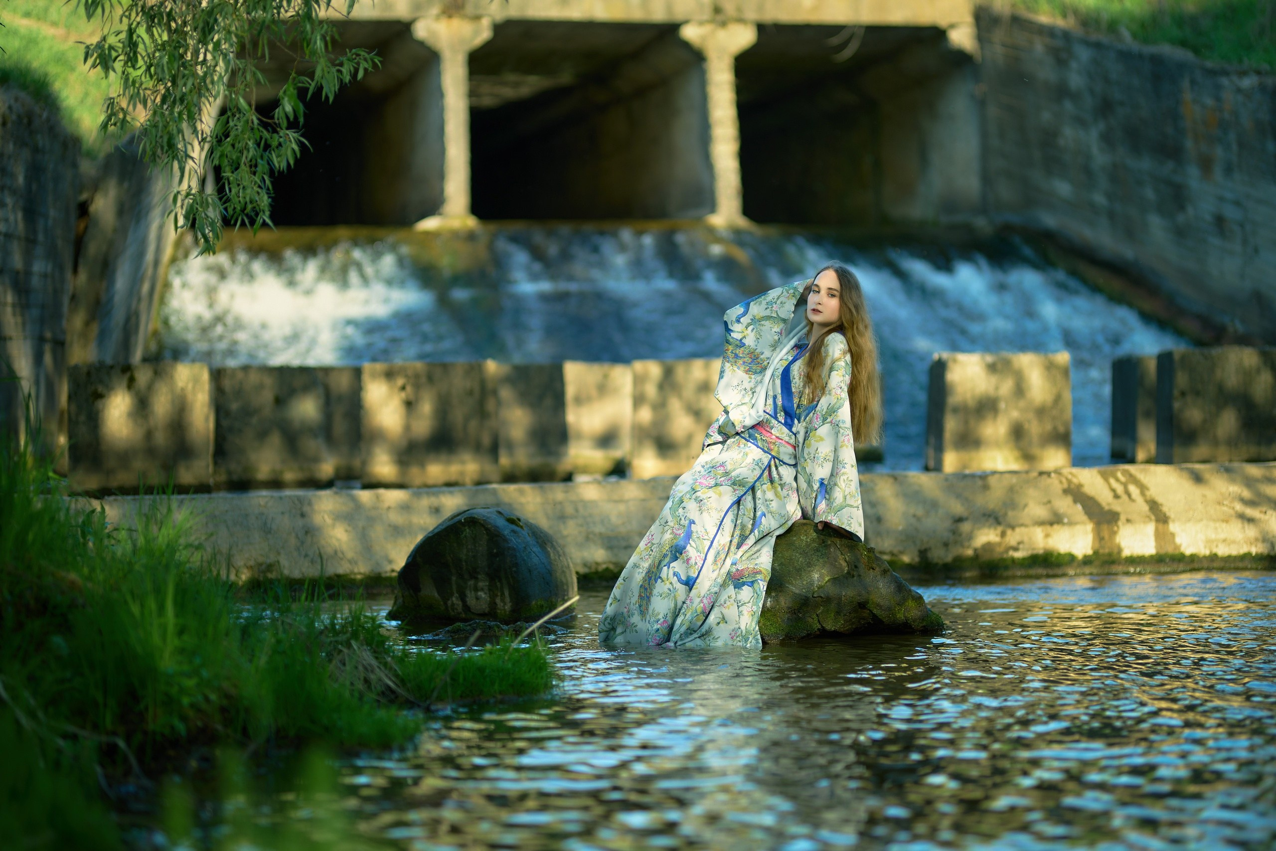 Девушка в светлом кимоно сидит на камне на фоне водопада