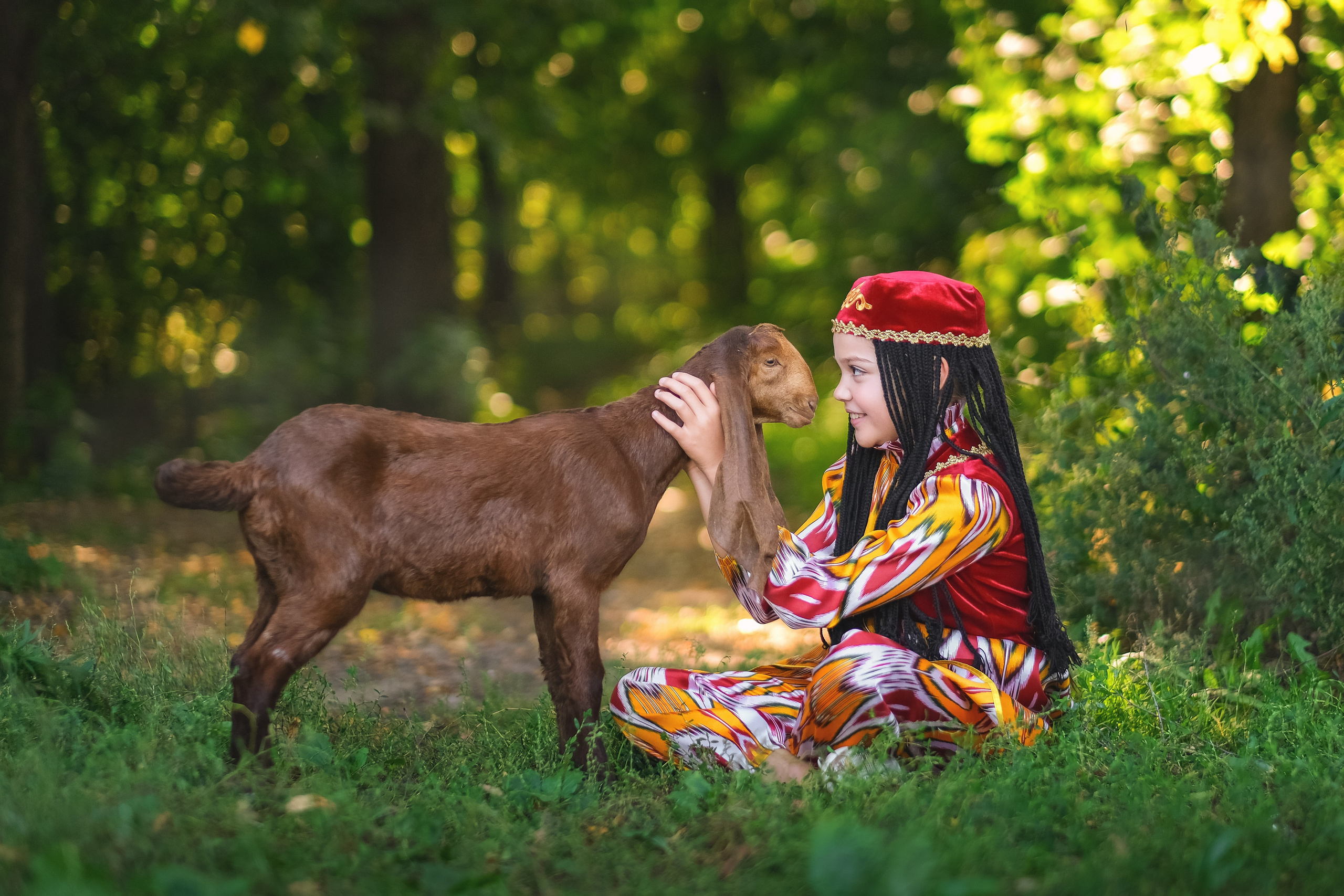 Девочка сидит на поляне с козликом