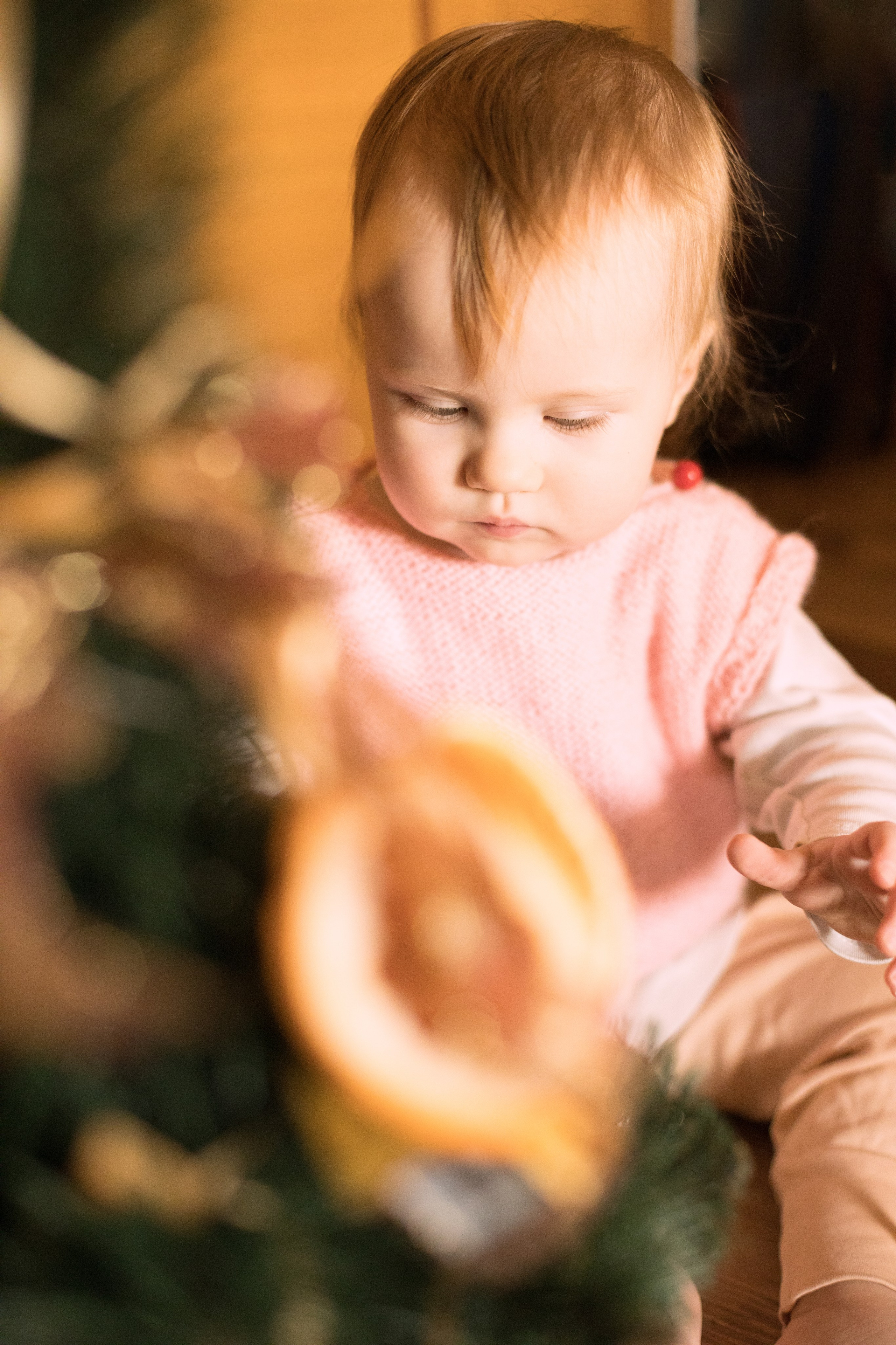 Маленькая девочка сидит рядом с ёлкой, украшенной сушеными апельсинами