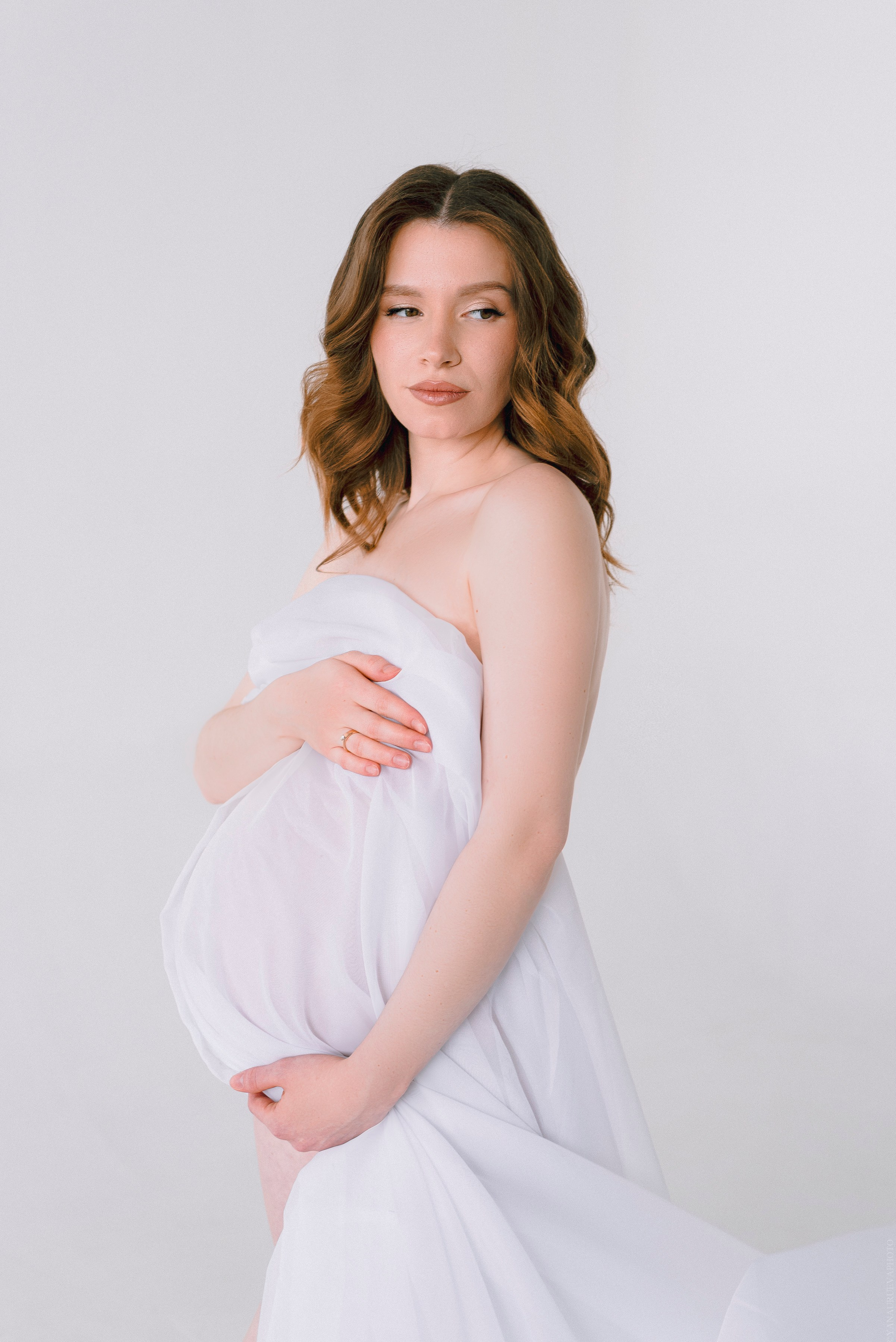 беременная девушка держит живот в белой ткани