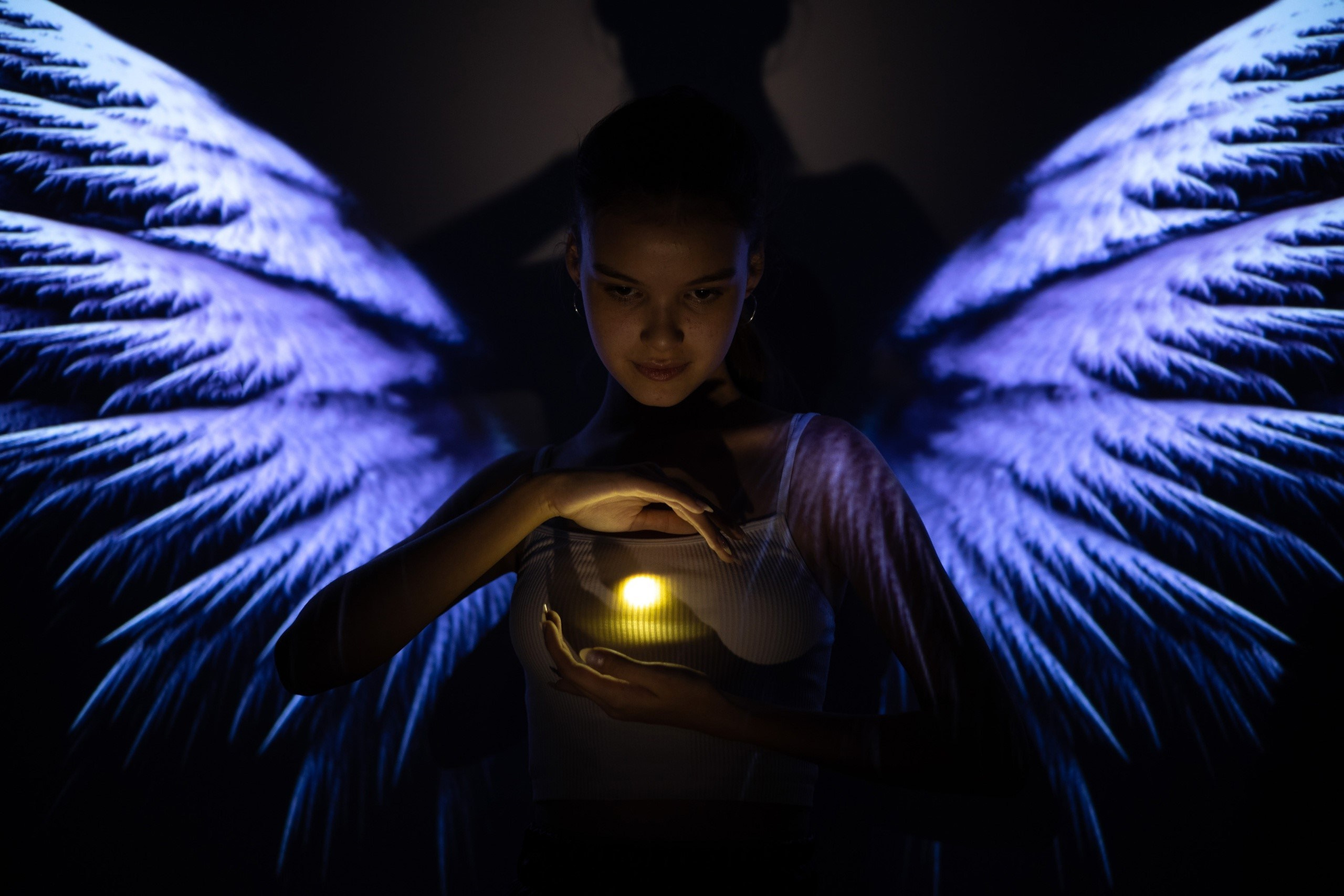 Проекторная съёмка Астрахань. Девушка на тёмном фоне, фиолетовые крылья и держит свет в руках.