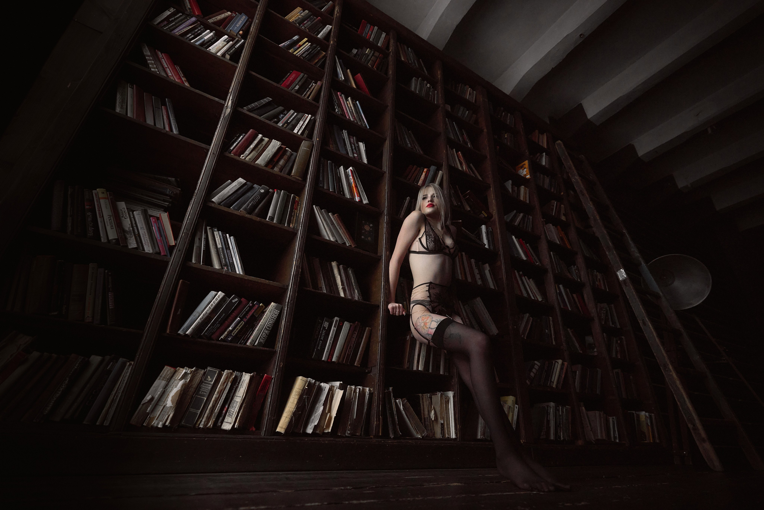 девушка у огромного книжного стеллажа позирует в чёрном нижнем белье