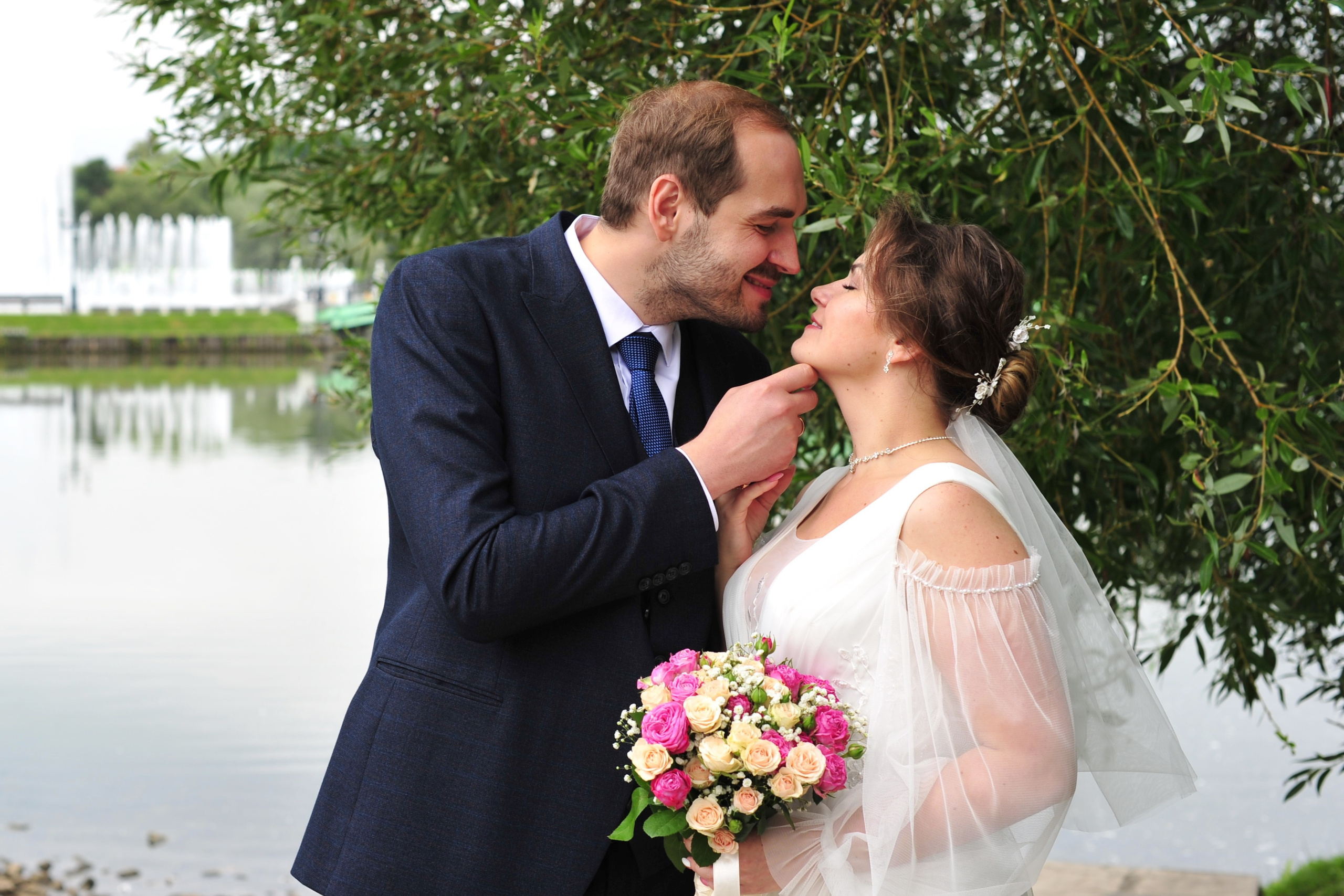 Свадьба в Царицыно пасмурным летним днем, жених и невеста смотрят друг на друга на фоне пруда и зеленой листвы