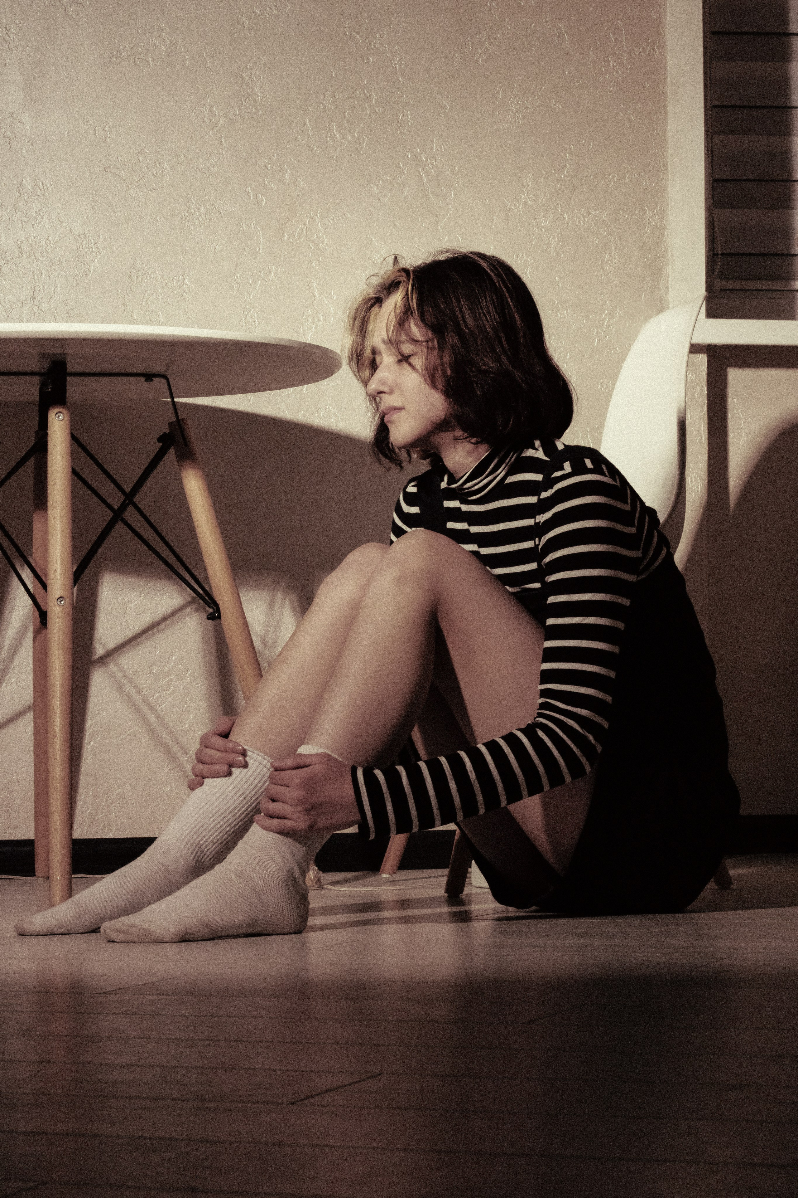 Девушка сидит на полу, уткнувшись в колени — воспоминания давят сильнее, чем тишина вокруг.