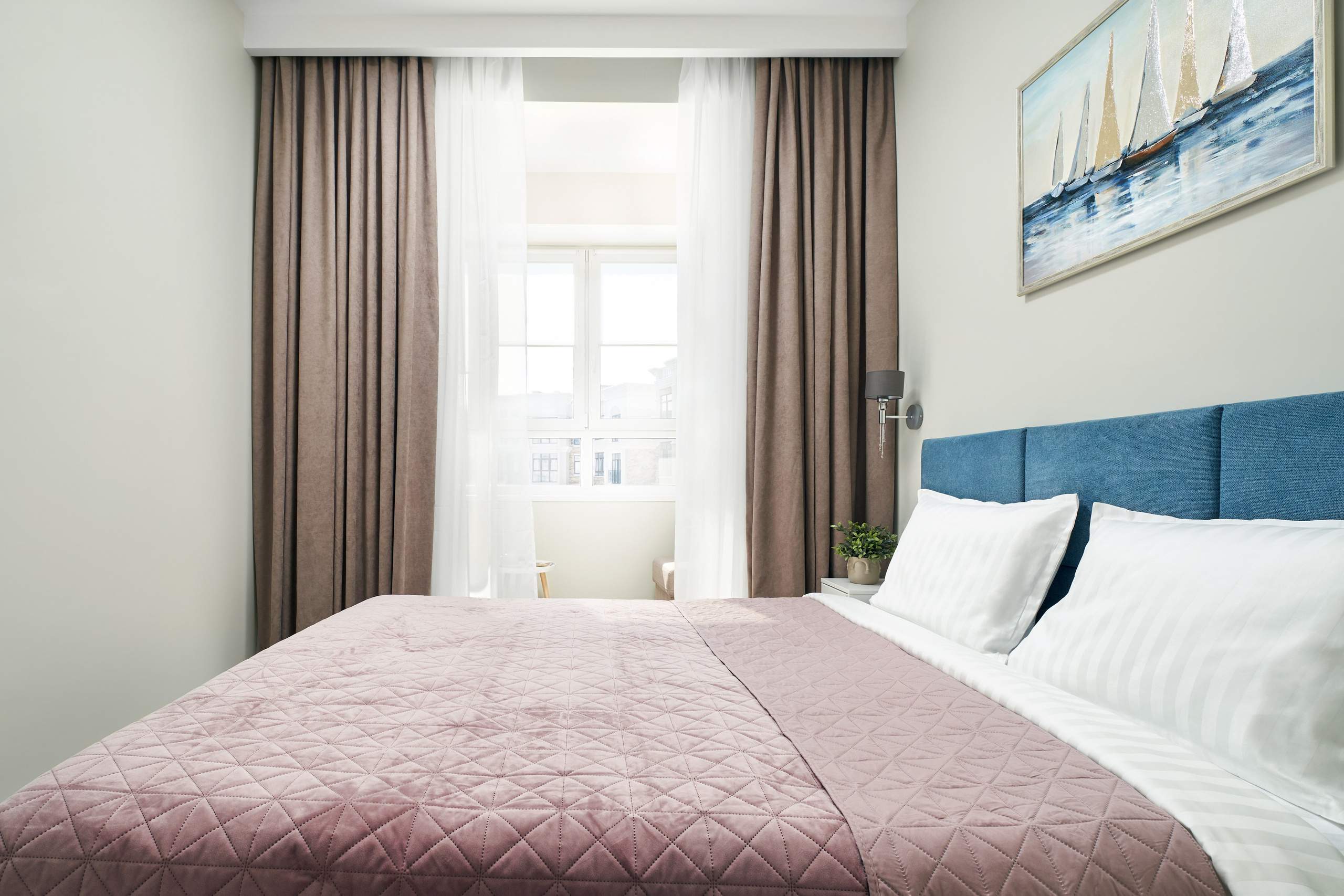 Спальня. Синее изголовье кровати, картина на стене, вид за окном