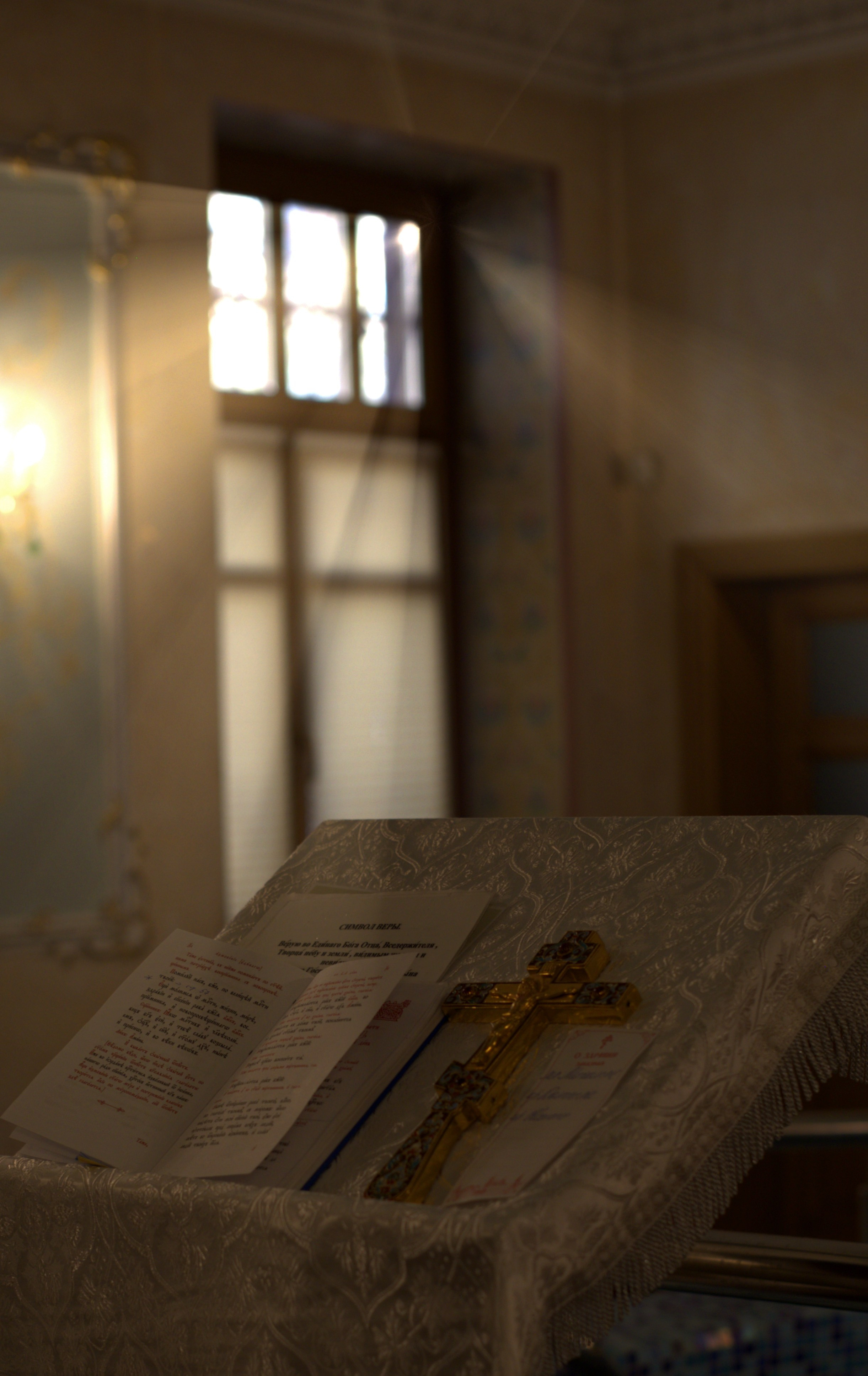 Открытый молитвослов с текстом Символа Веры и золотой крест на столике в храме перед таинством крещения