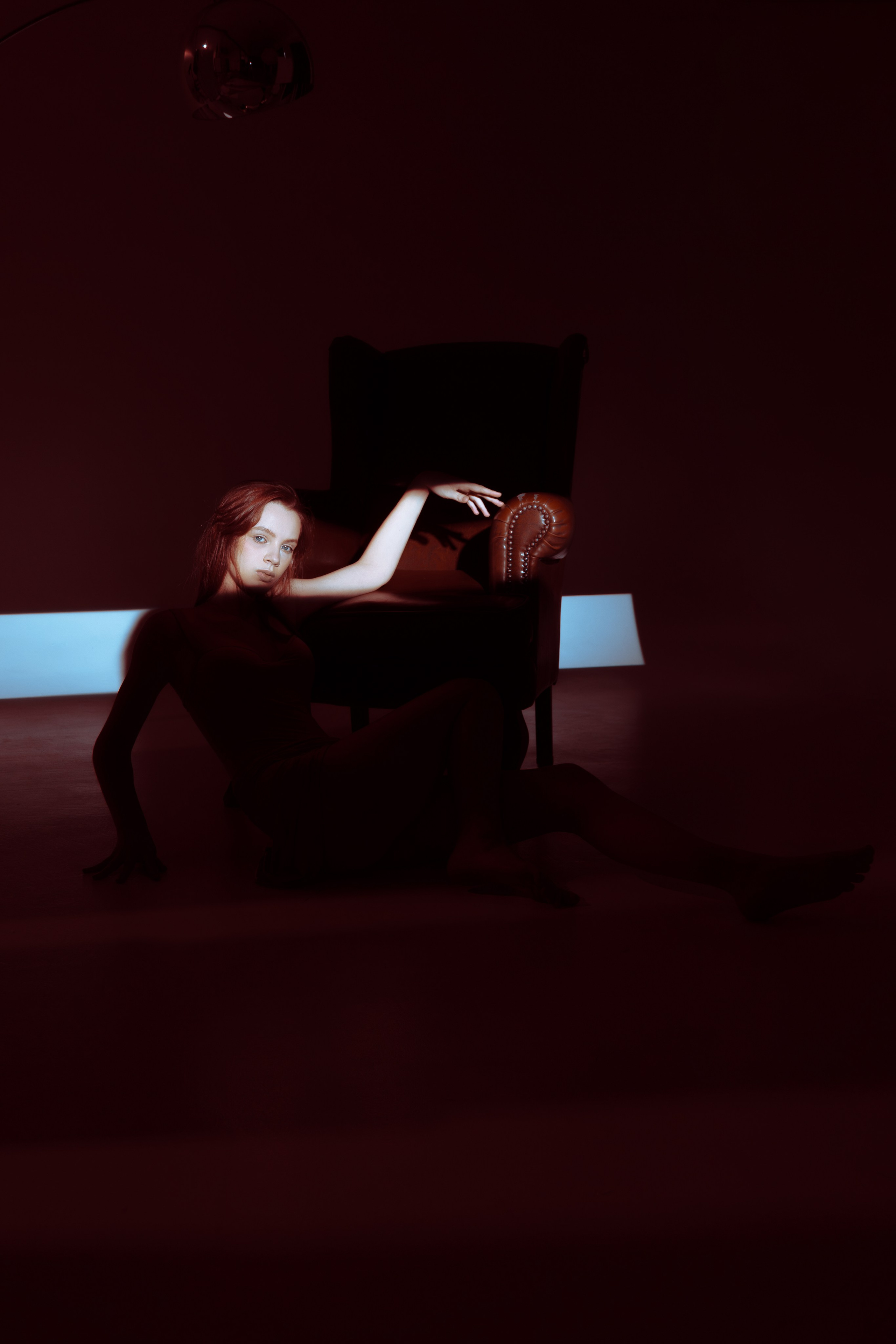 Студия, кресло, вдохновение: модель в нежном платье словно погружена в свои мысли. Геометрические световые пятна на стене добавляют композиции художественности.