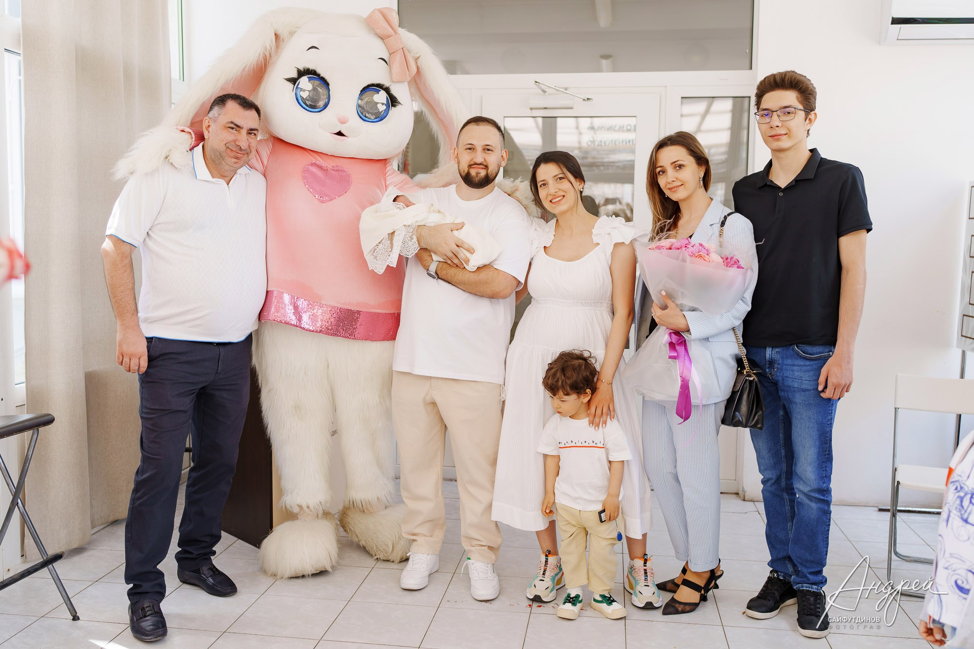 Молодые родители с новорожденной на фотозоне роддома ЦГБ в окружении гостей и ростовой куклы, Ростов-на-Дону, фотосъемка выписки