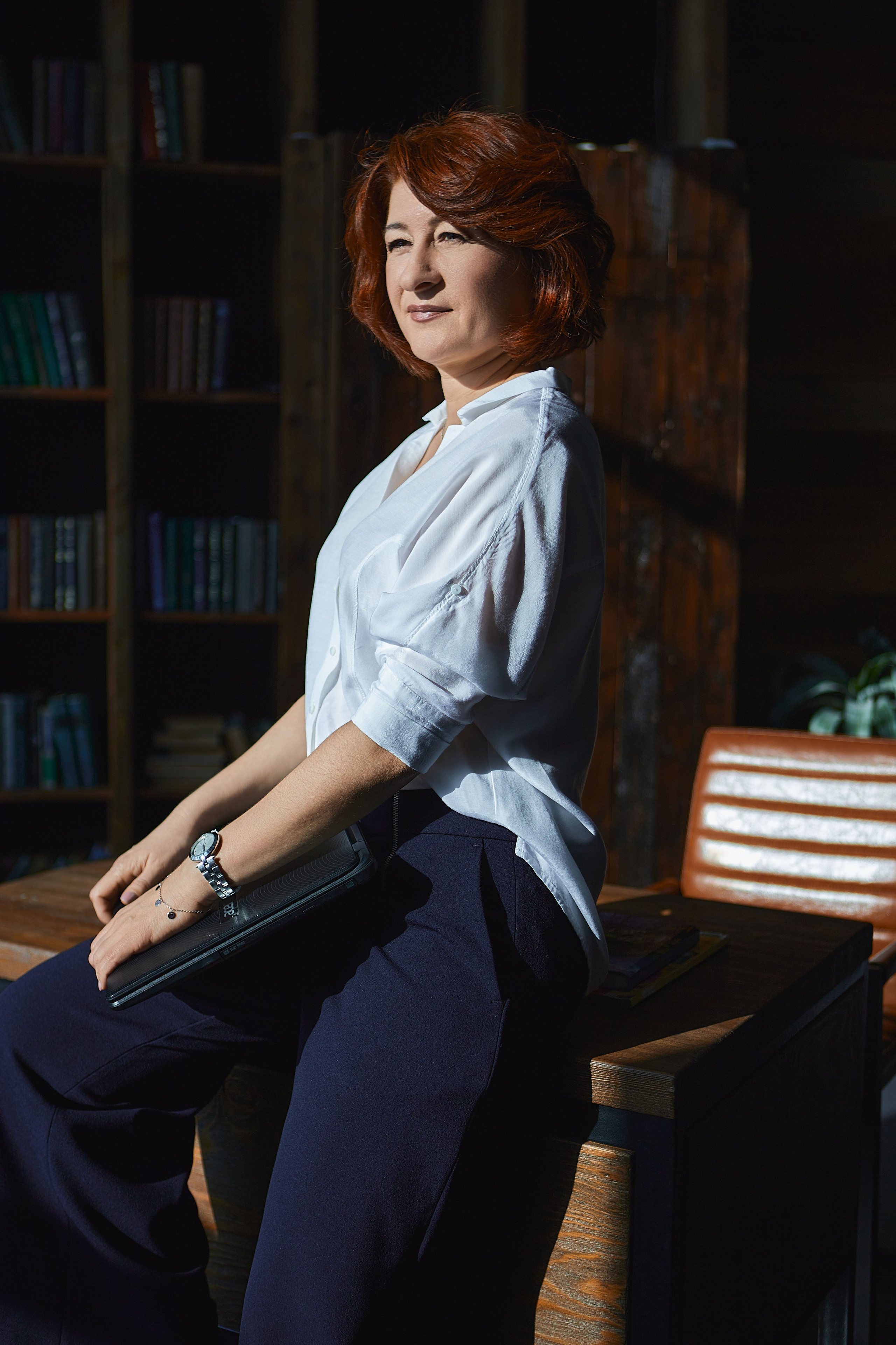 Деловая женщина с ноутбуком облокотилась на письменный стол в библиотеке