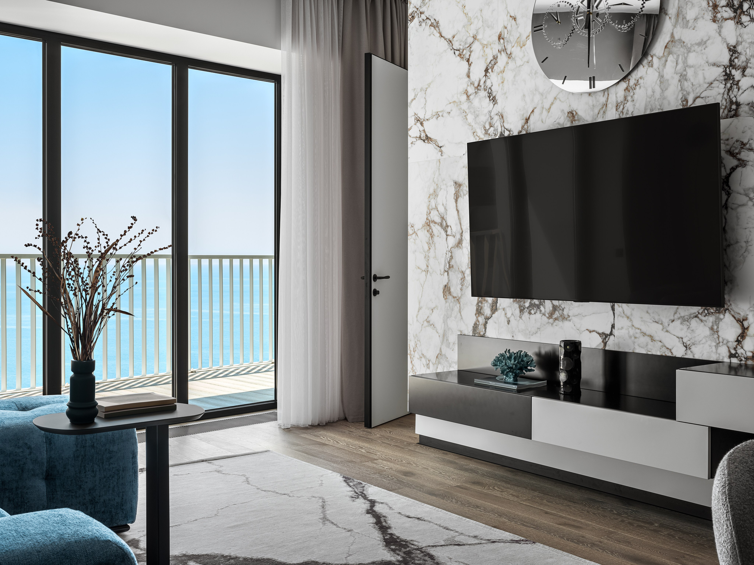 Интерьер гостиной с акцентной мраморной стеной и встроенным телевизором, дополненный минималистичной мебелью и панорамным видом на море; проект Рената Байчукова и Алеси Кириенко, стилист Екатерина Ракитина, фотограф Сергей Денисенко.