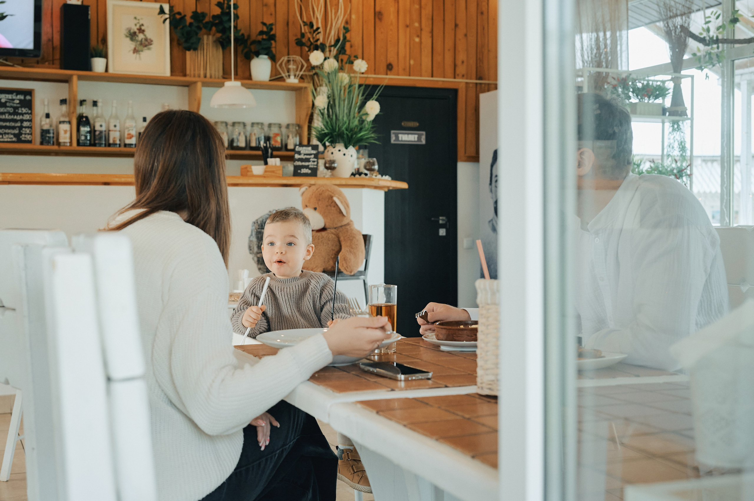 Мальчик с родителями сидит за столиком в кафе, оживлённо говорит, держит ложку.