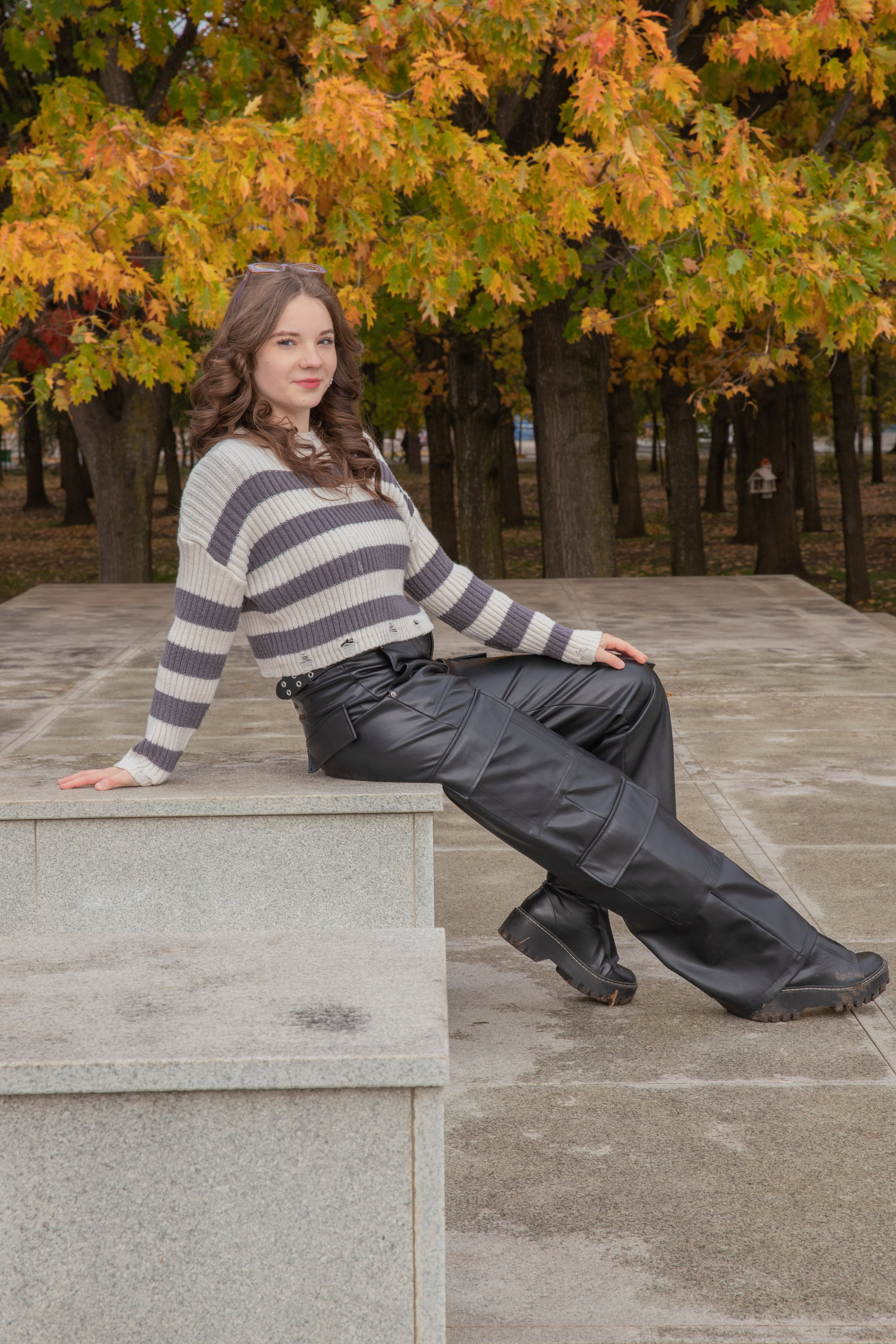 Осенняя прогулка: девушка в кожаных черных брюках на фоне живописной природы парка Чистяковская роща, где листья становятся ярко-оранжевыми.