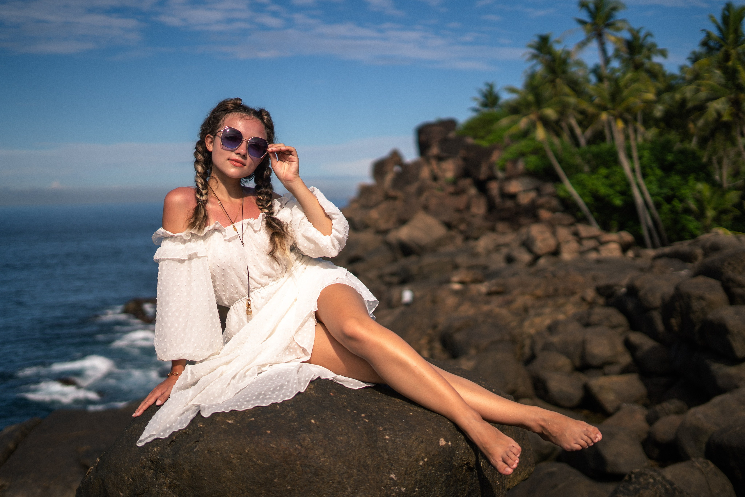 a girl in a white dress and glasses against the backdrop of turquoise ocean water