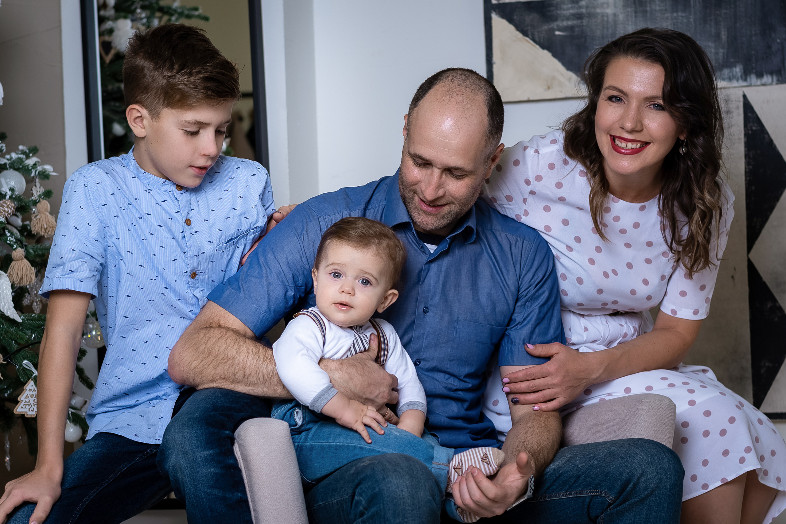 семья из четырех человек сидя на кресле возле елки