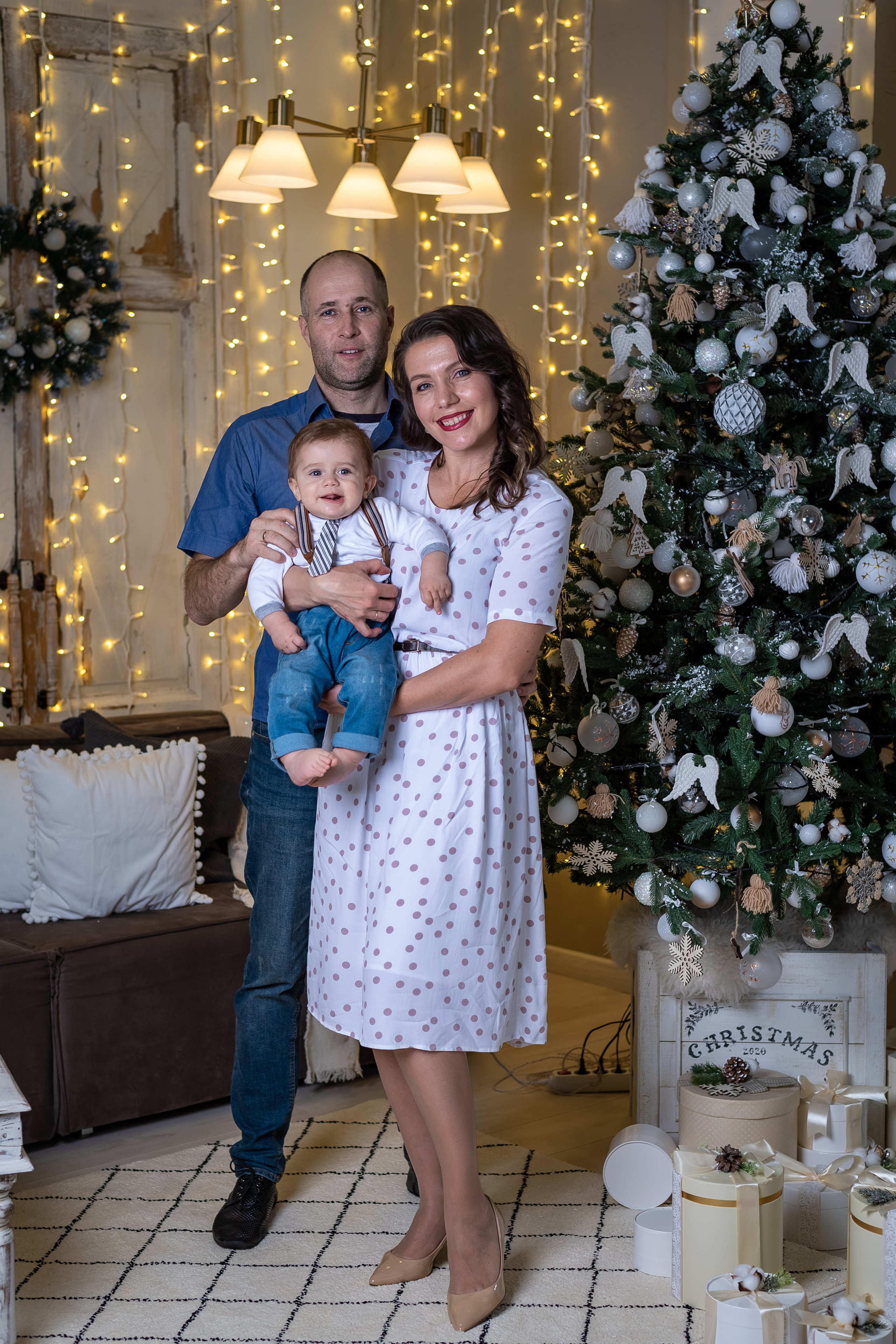Семья с маленьким ребенком стоя у новогодней елки.