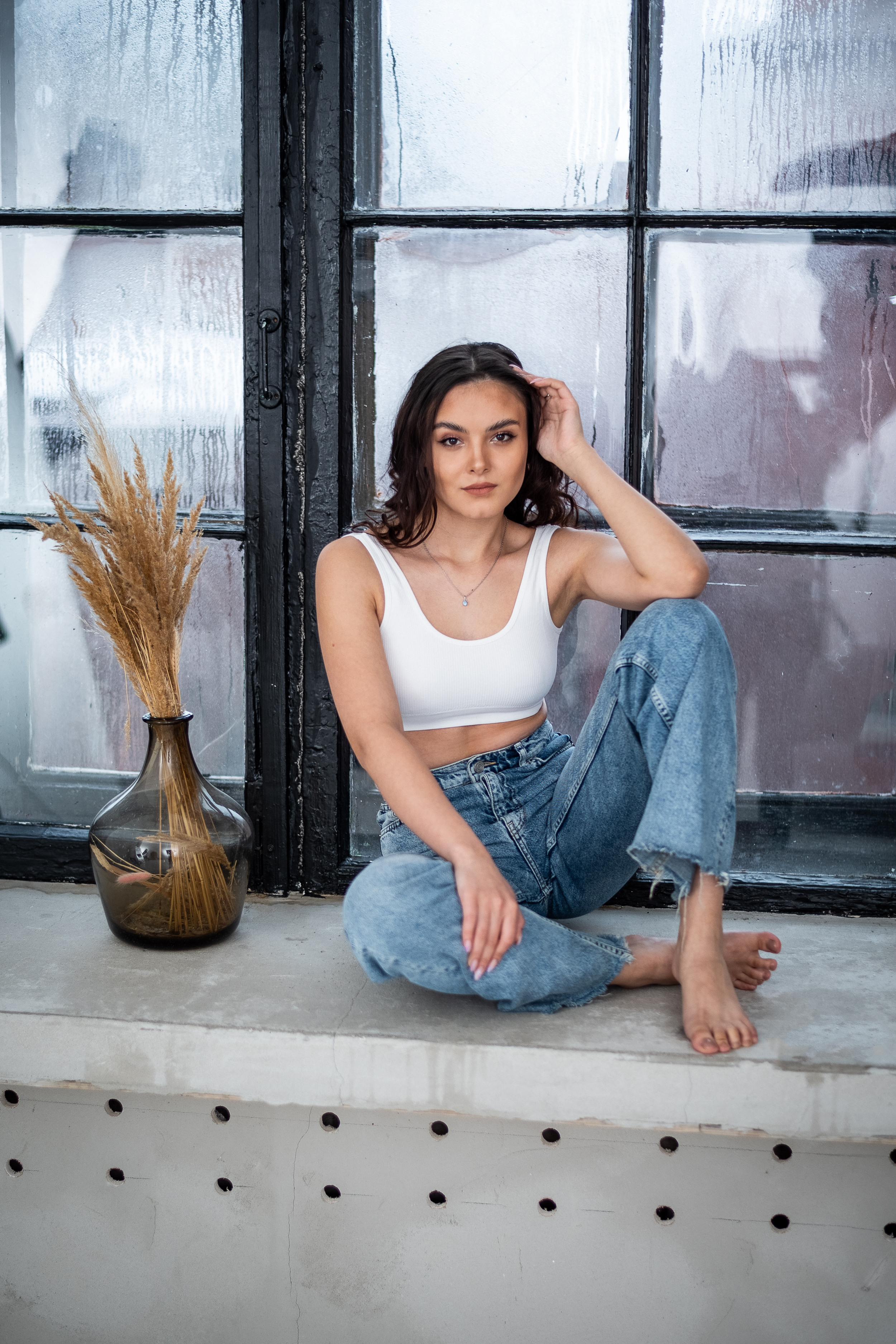 девушка сидя на окне рядом ваза с свухоцветом.