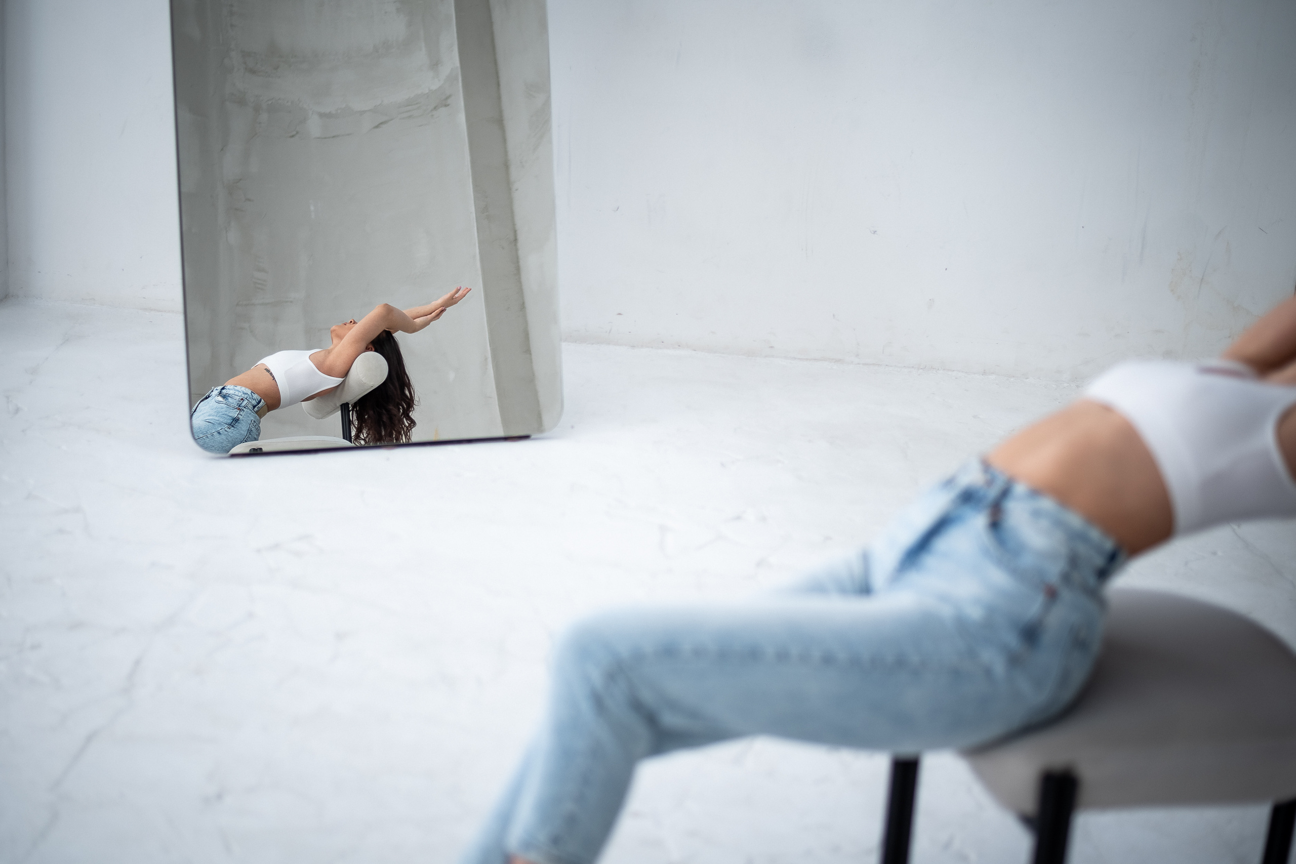 отражение девушки в зеркале в стиле минимализма, которая выгнулась на стуле