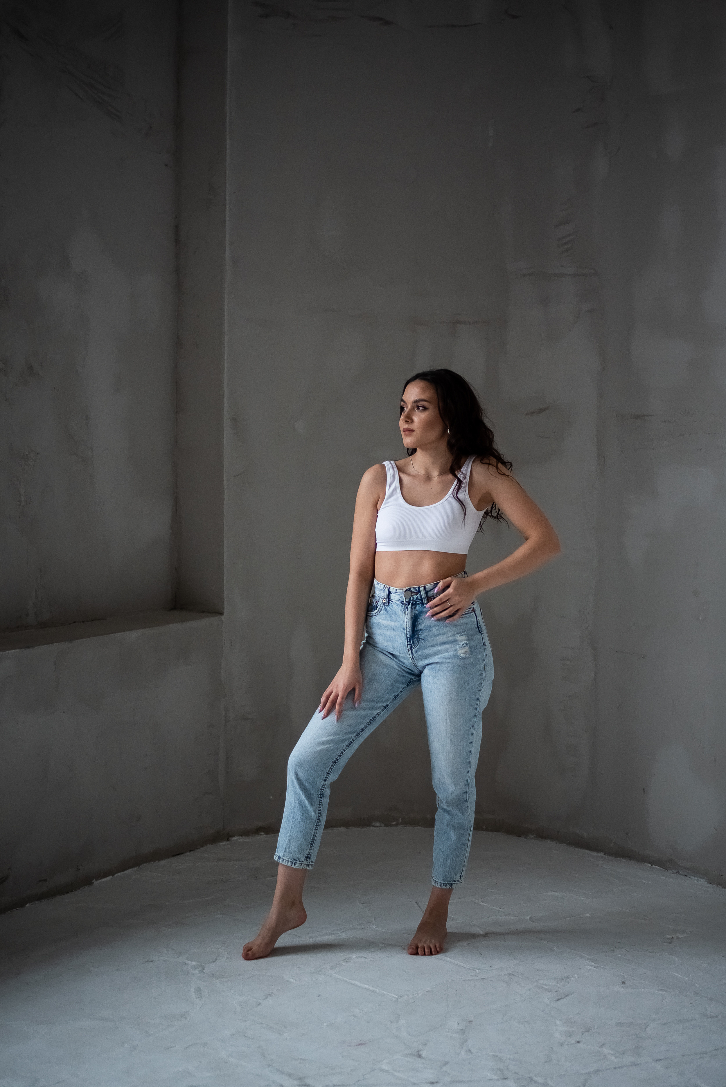 девушка в джинсах и светлом топе на задрнем плане серая стена