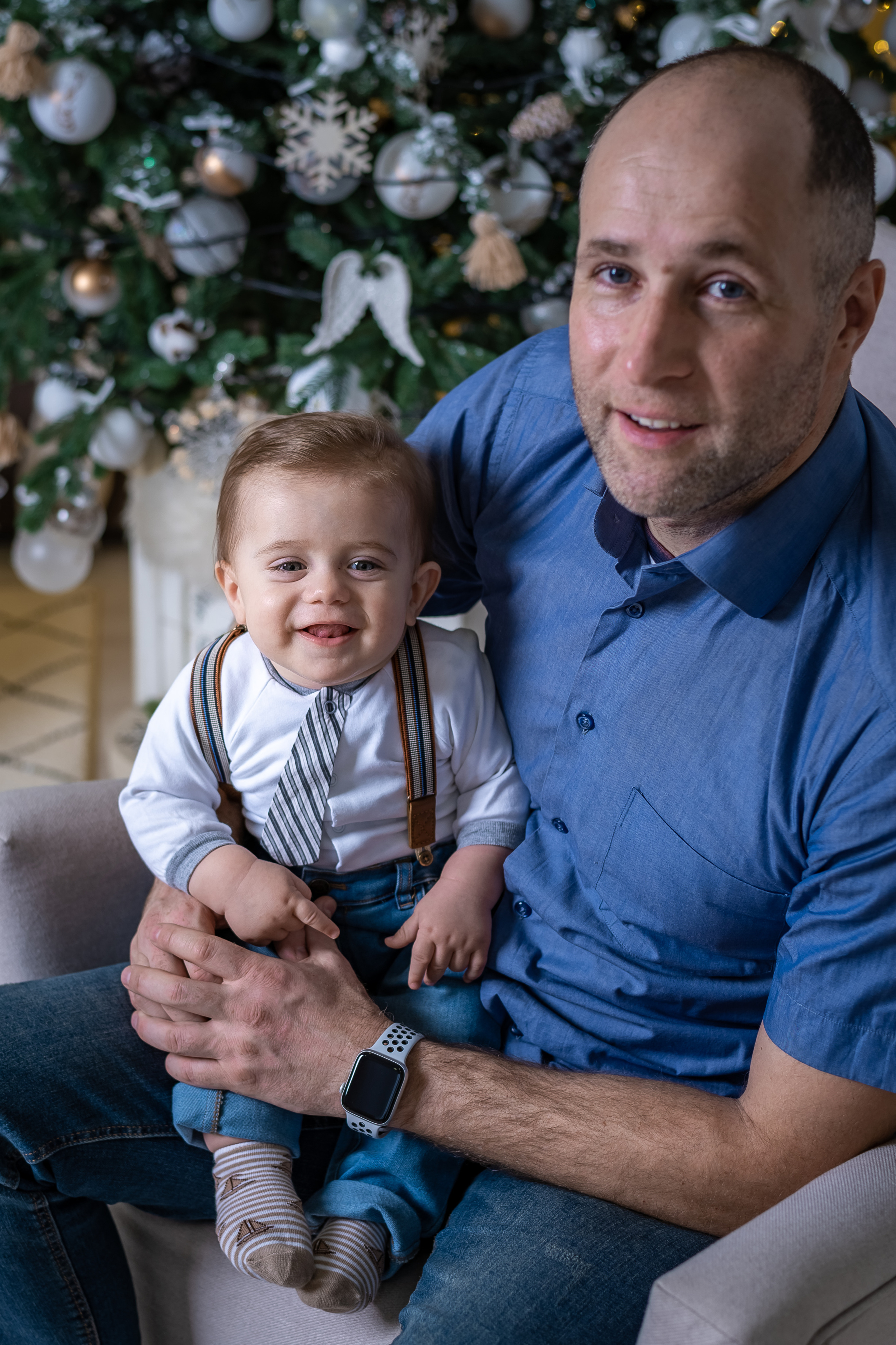 Папа в голубой рубашке с сыном на коленях. На заднем плане новогодняя елка.