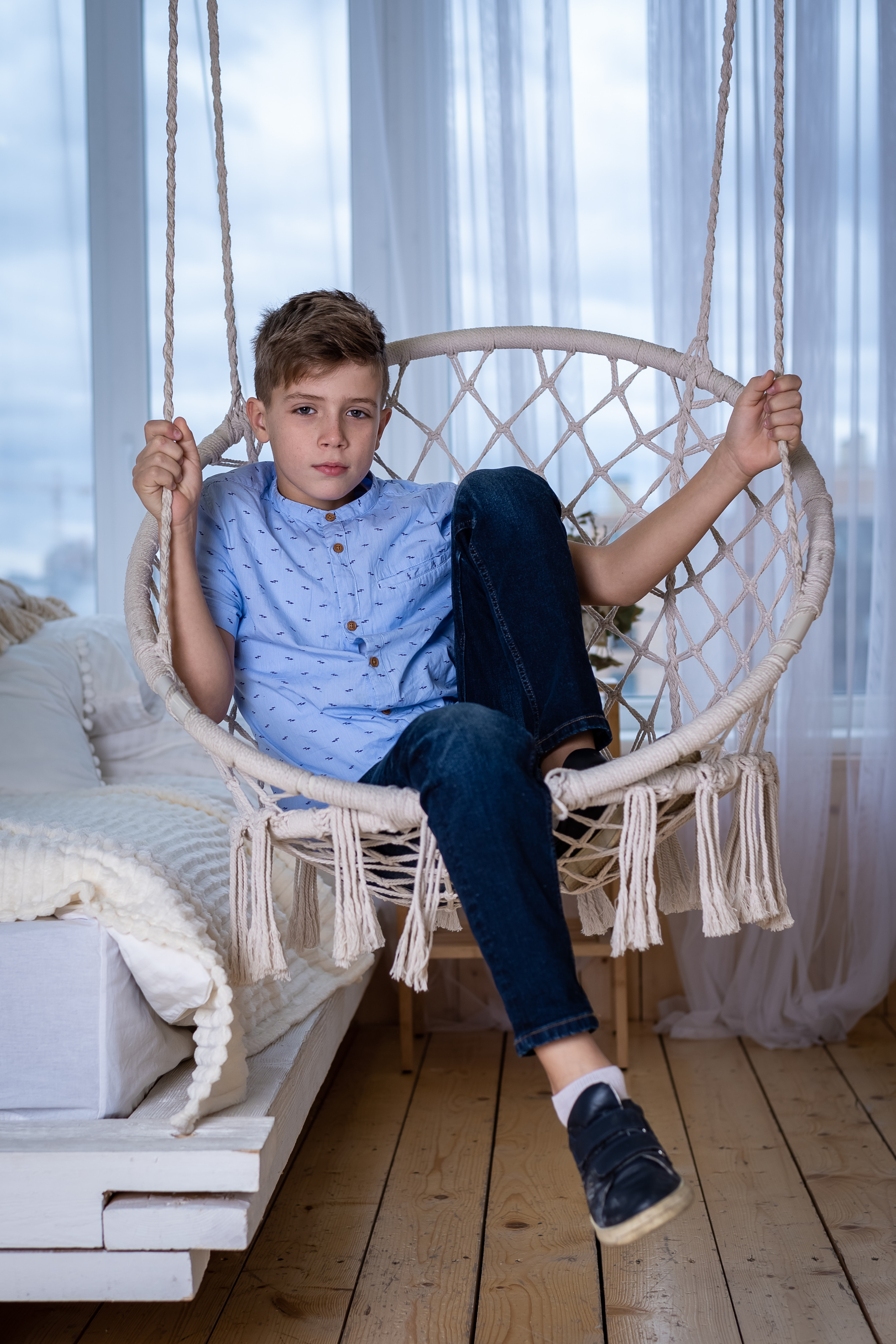 мальчик на подвесных качелях на фоне окна
