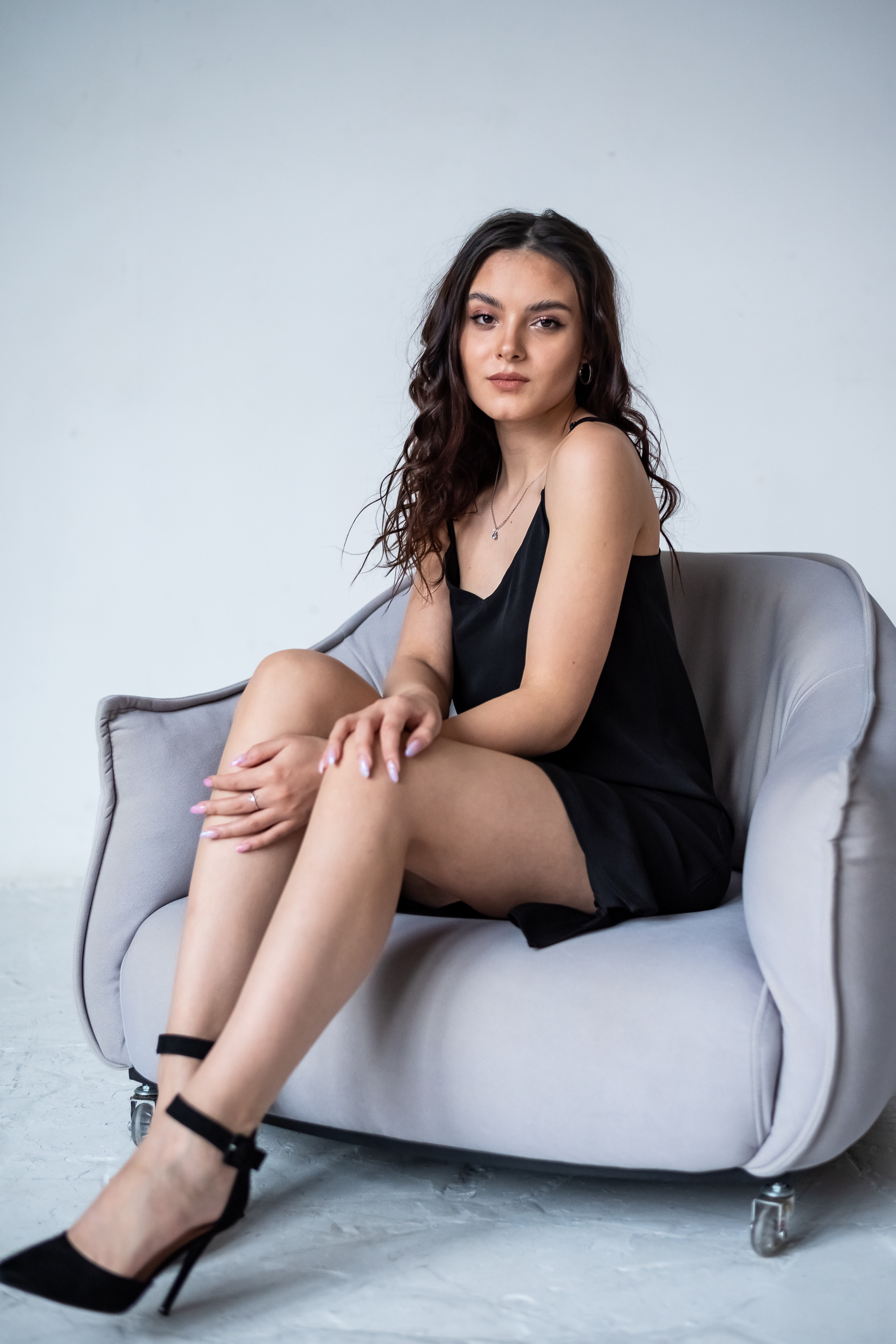 девушка в темном платье в сером кресле на фоне белой стены