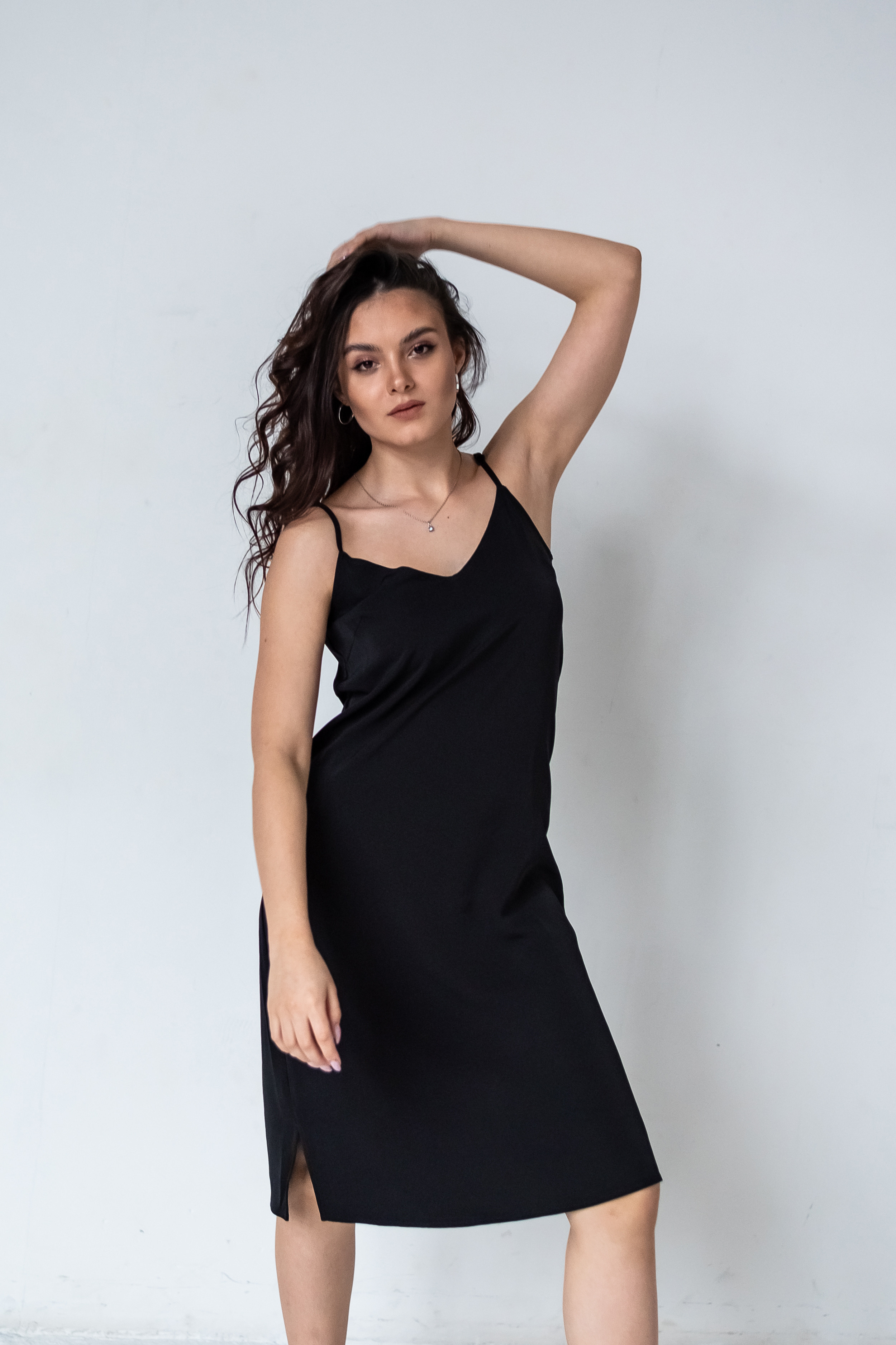 девушка стоя около светлой стены в темном платье