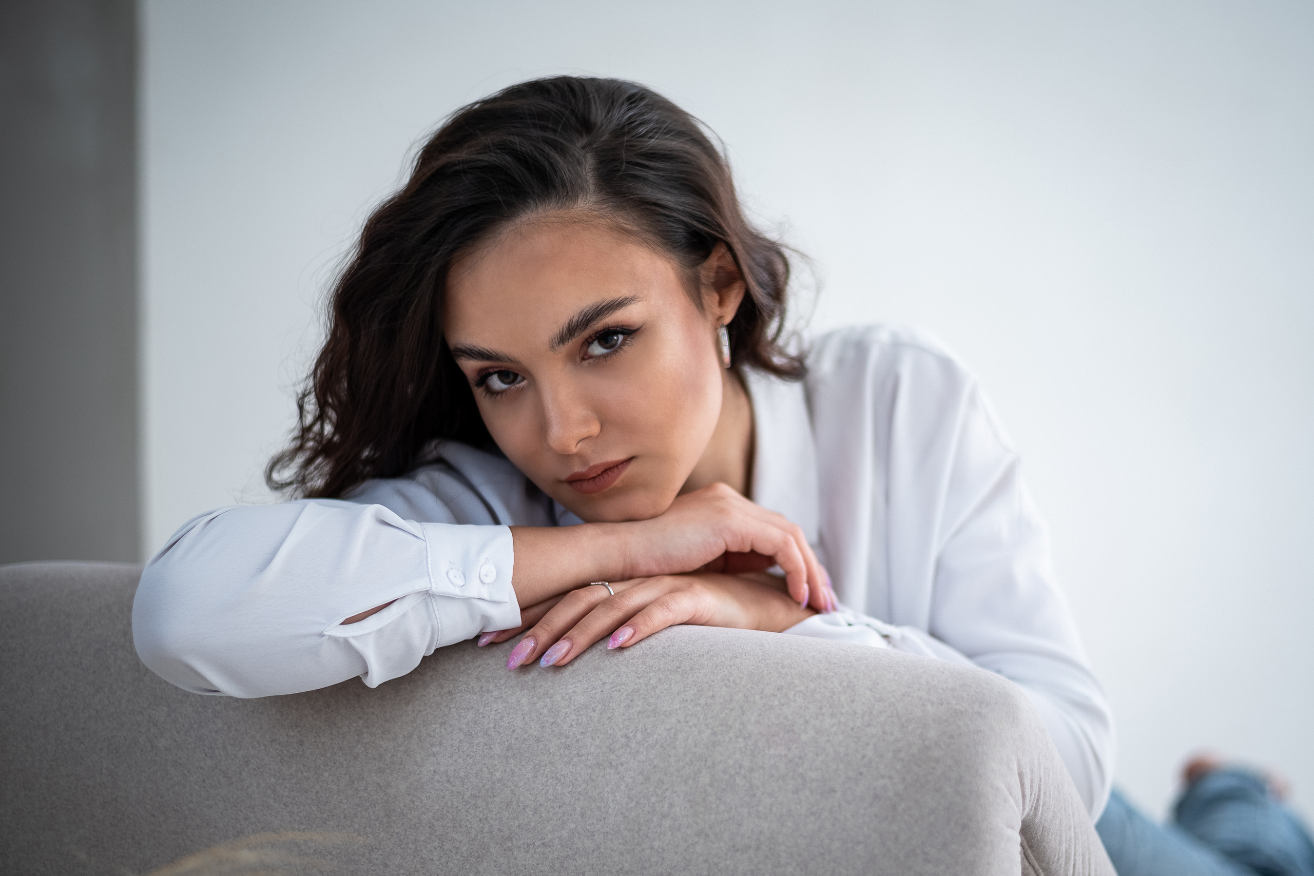 портрет девушки положившей голову на руки на фоне светлой стены