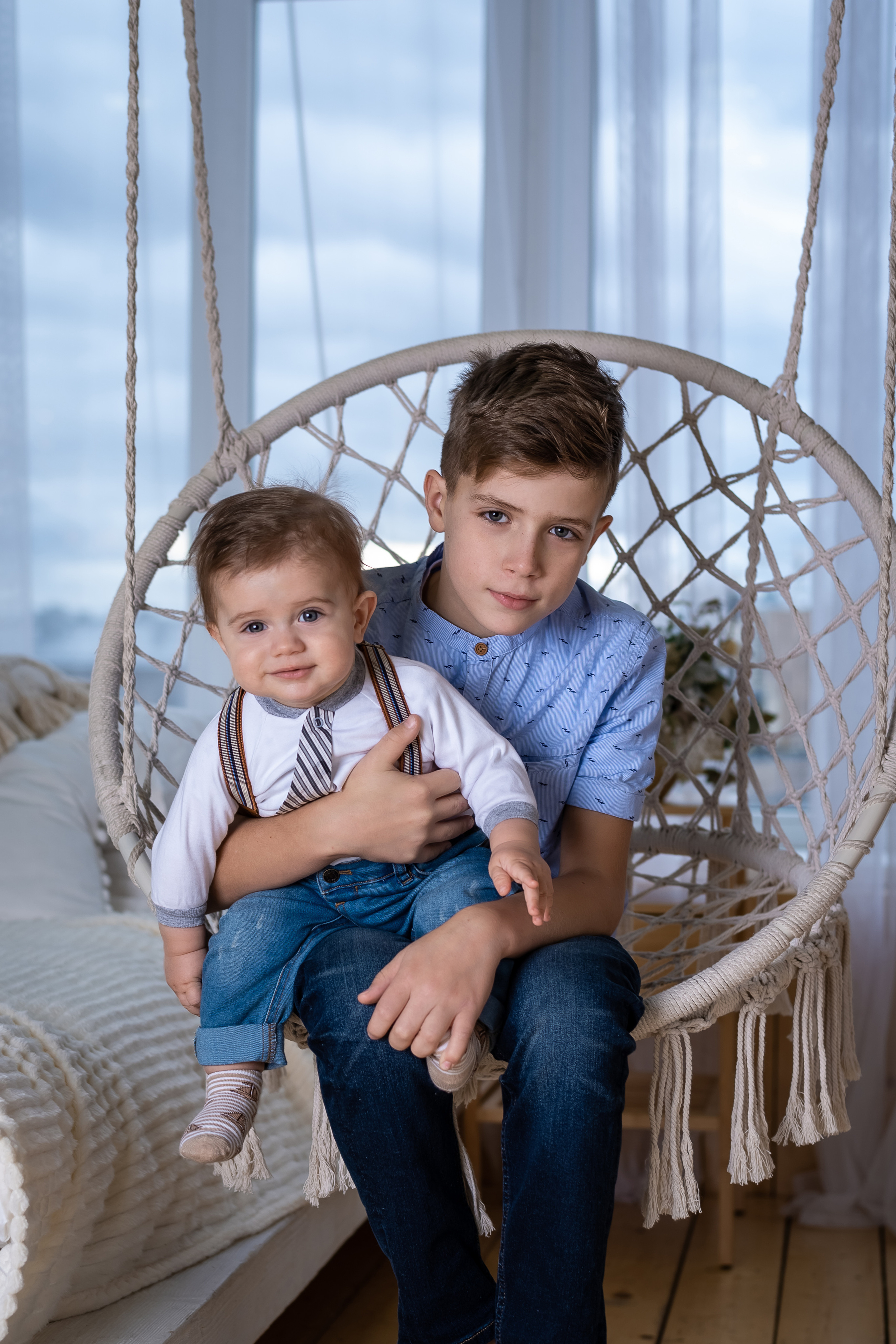 братья на подвесном кресле с окном на заднем плане