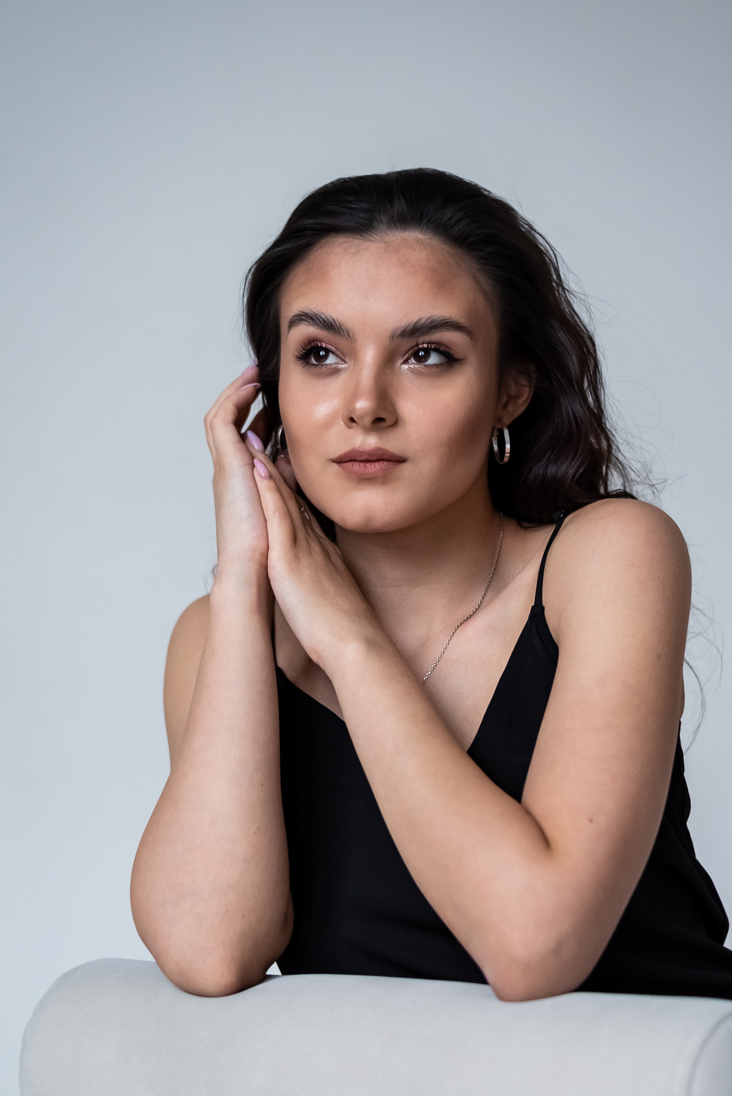 портрет девушки с вьющимися волосами и руками около лица