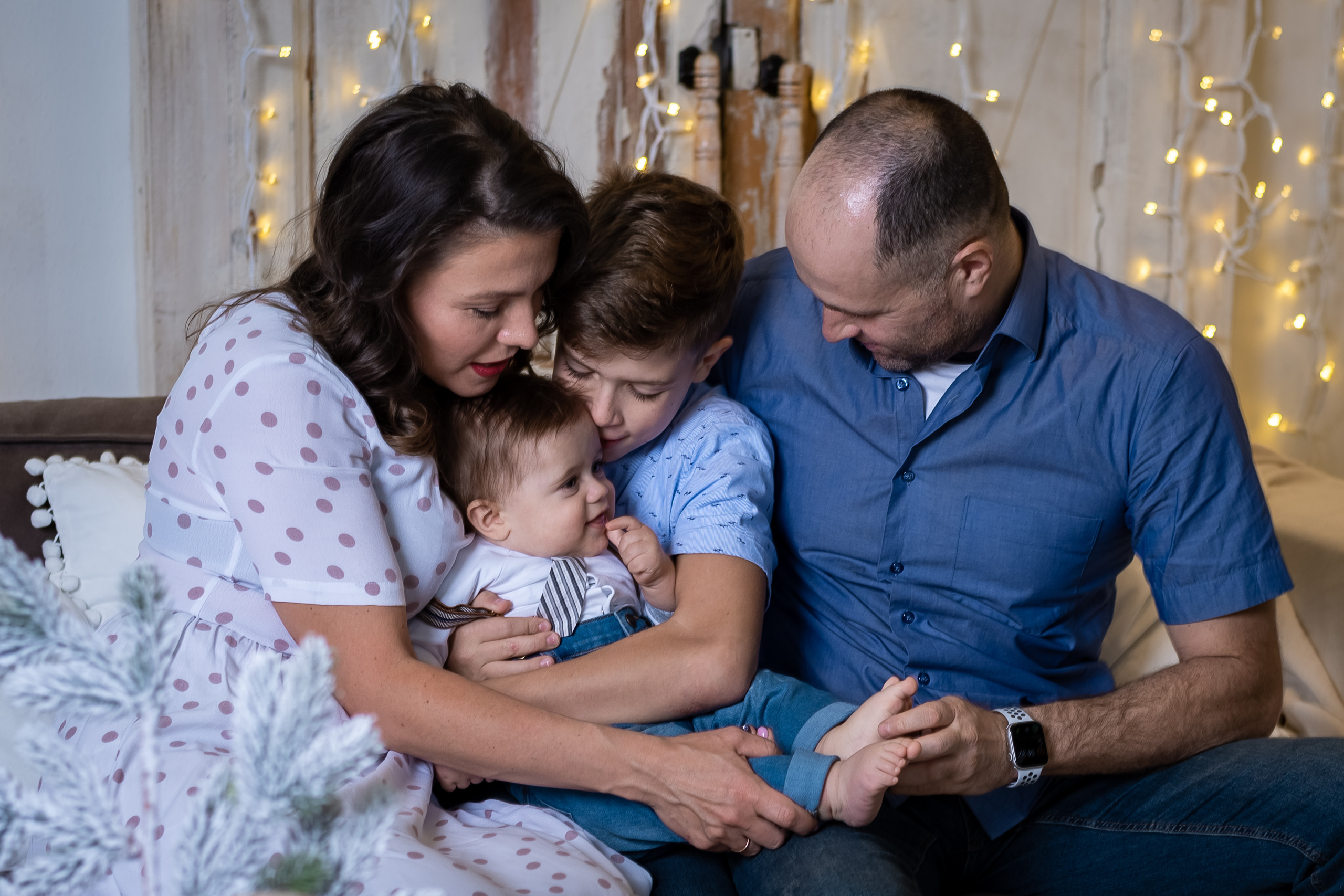семья с двумя сыновьями на диване, все смотрят на малыша