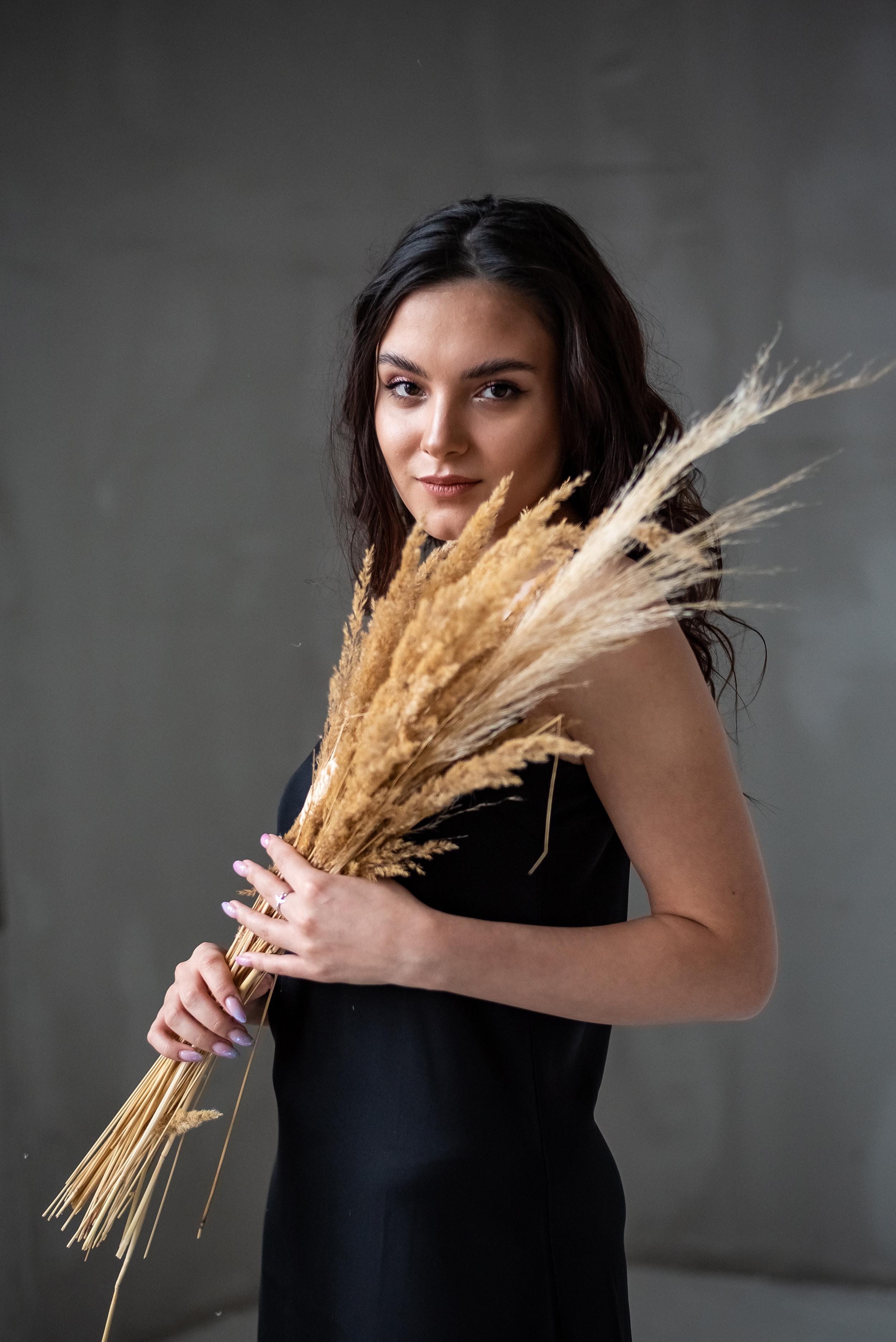 девушка в платье стоя у окна с сухоцветами в руках 