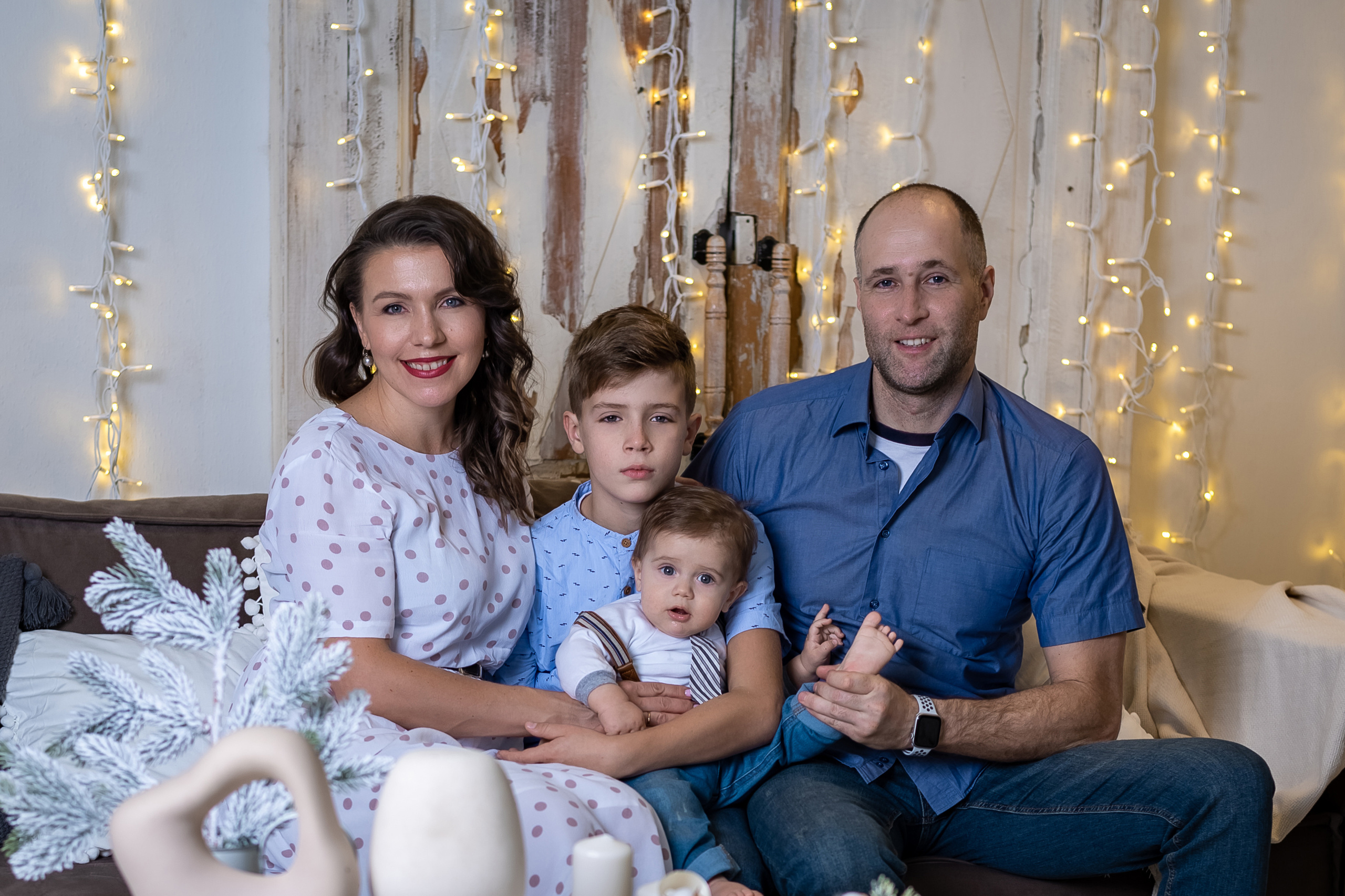 семья из четырех человек с двумя сыновьями сидя на диване на фоне светлой стены.