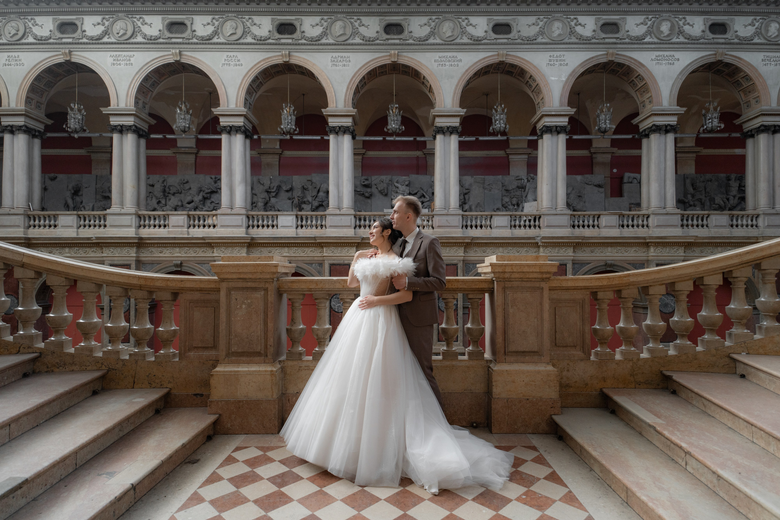 Жених обнимает невесту на свадебной фотосессии на лестнице в академии Штиглица в Санкт-Петербурге