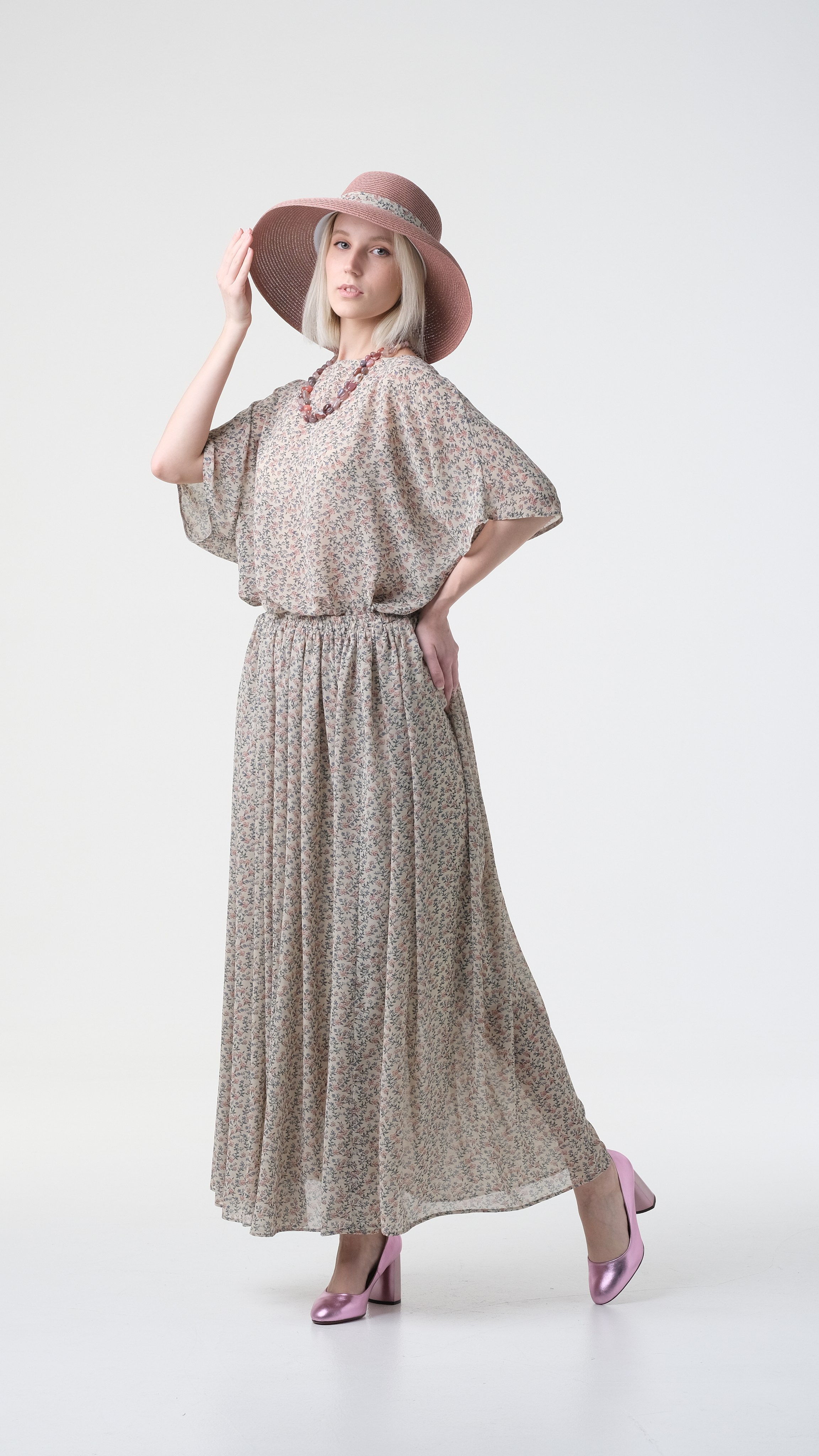 Девушка в динамике шагает и держится за шляпу. Светлое платье, красивая модель.