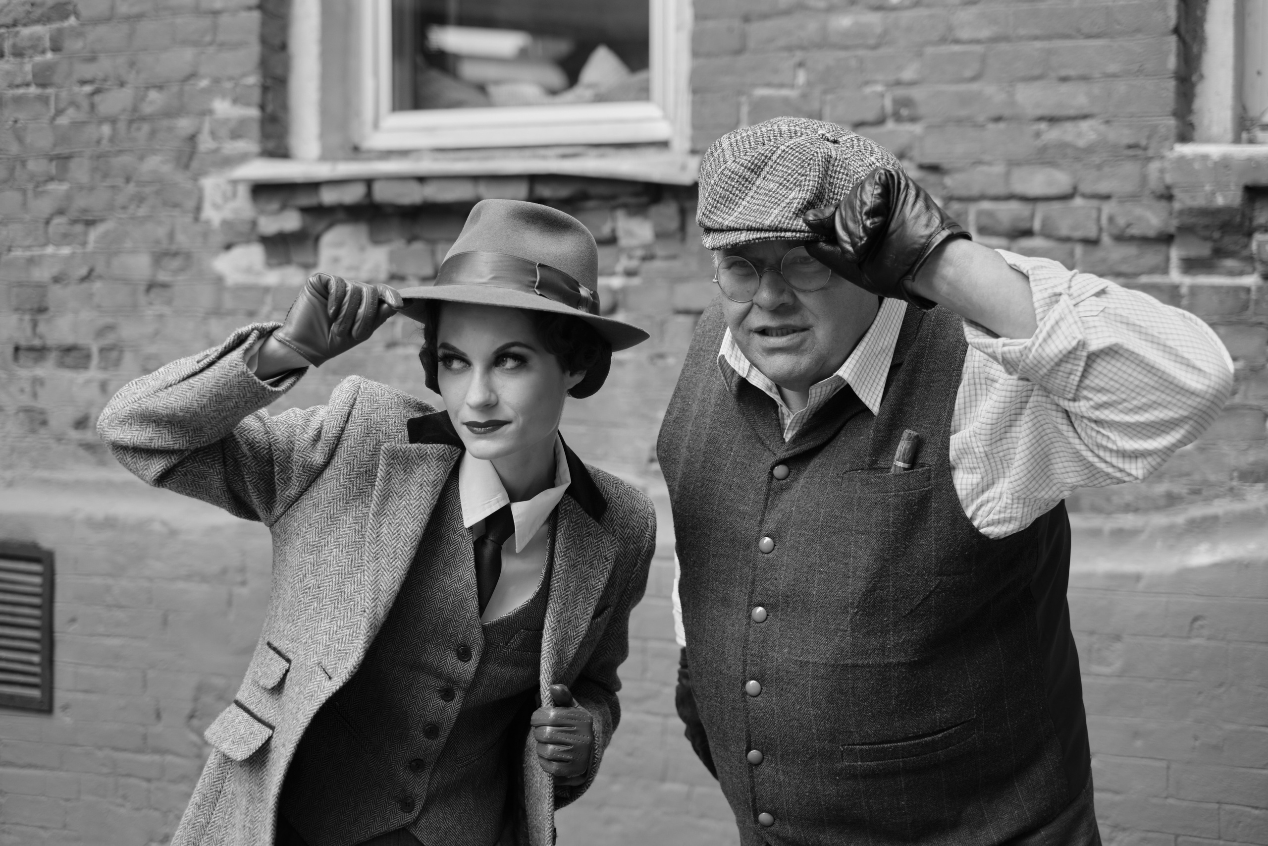 Девушка и мужчина в классических костюмах смотрят в даль держась за шляпы