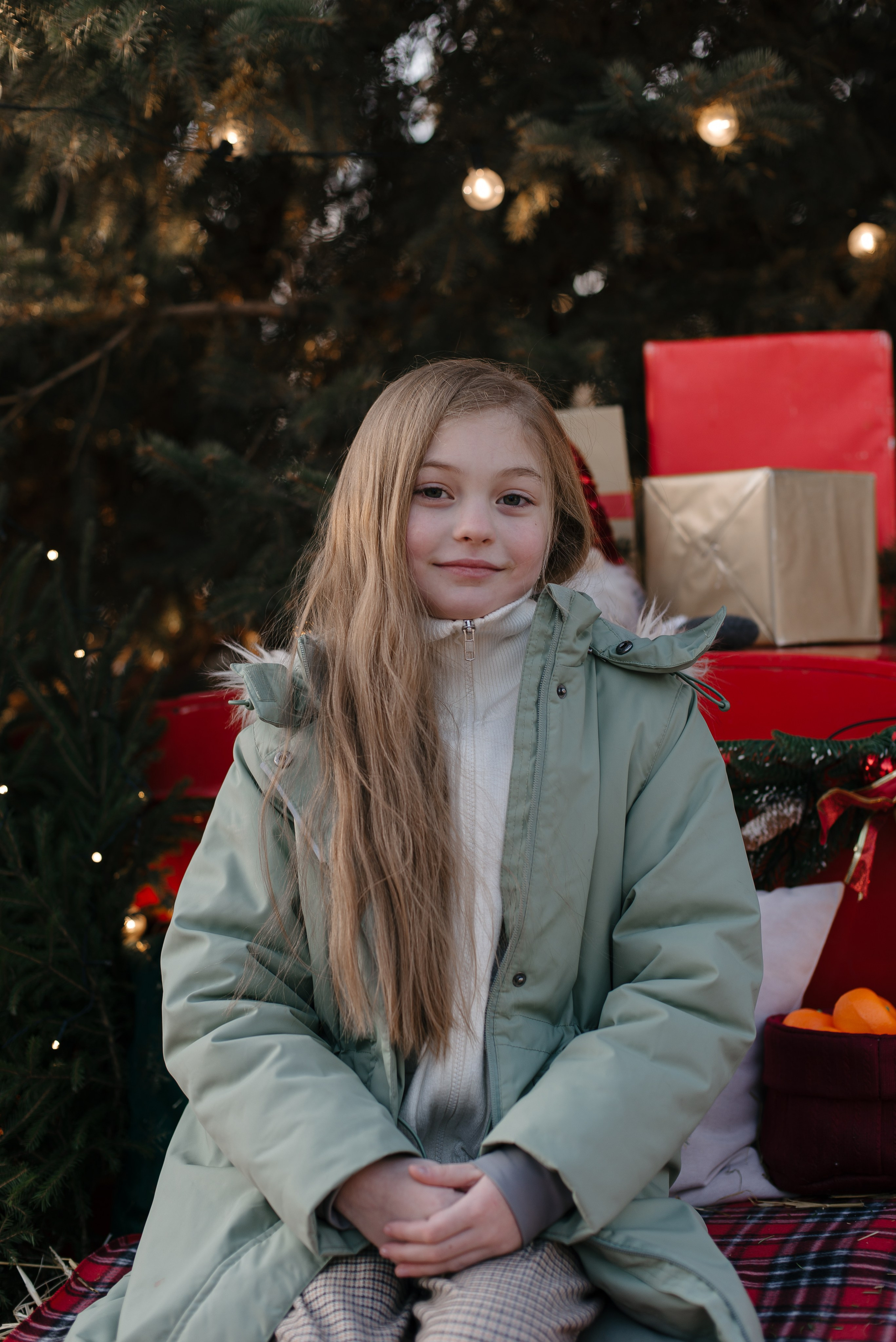 Девочка в зеленой куртке на фоне елки.