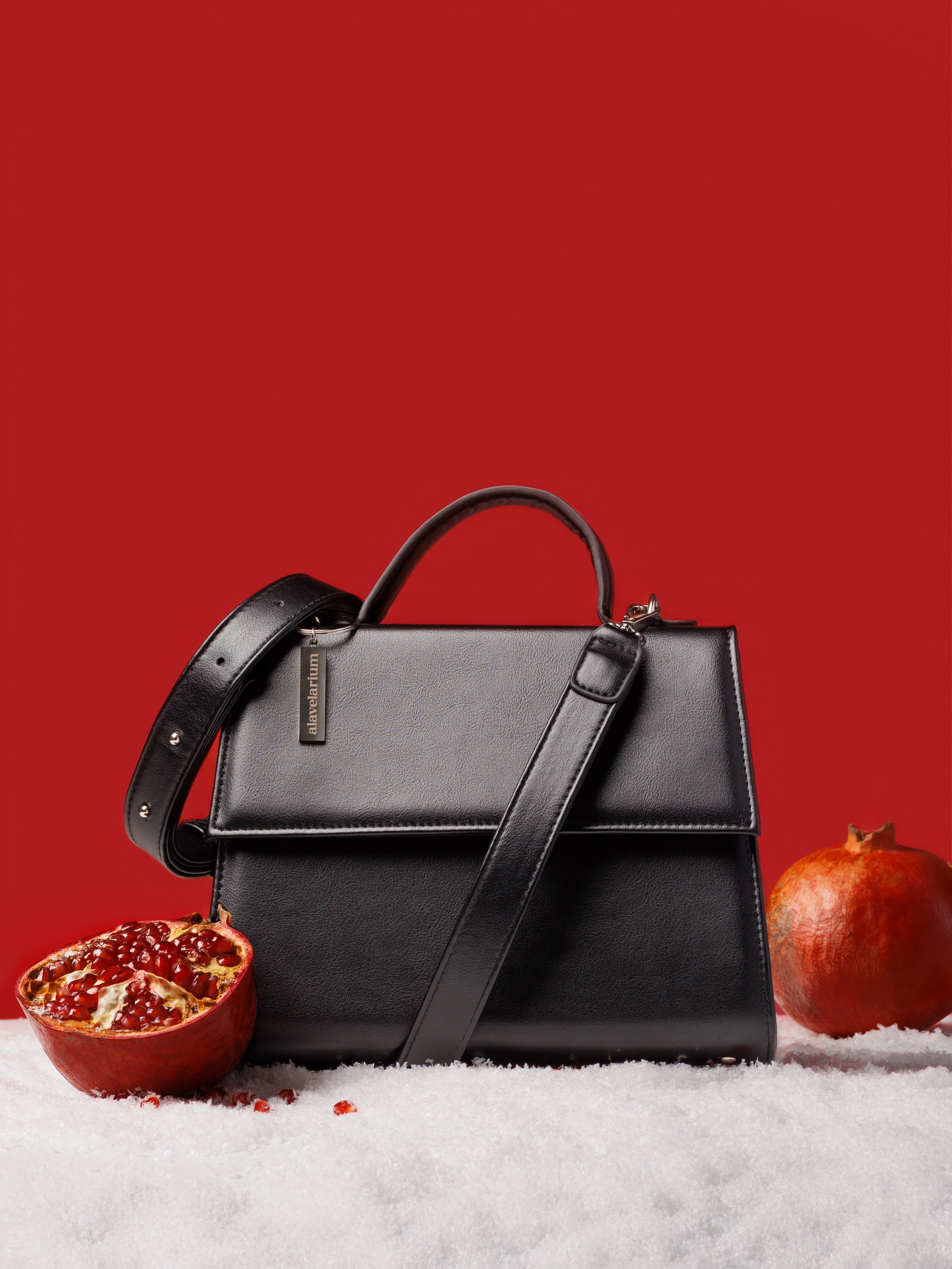 Черная женская сумка на снегу с гранатами на красном фоне. Рекламная съемка.