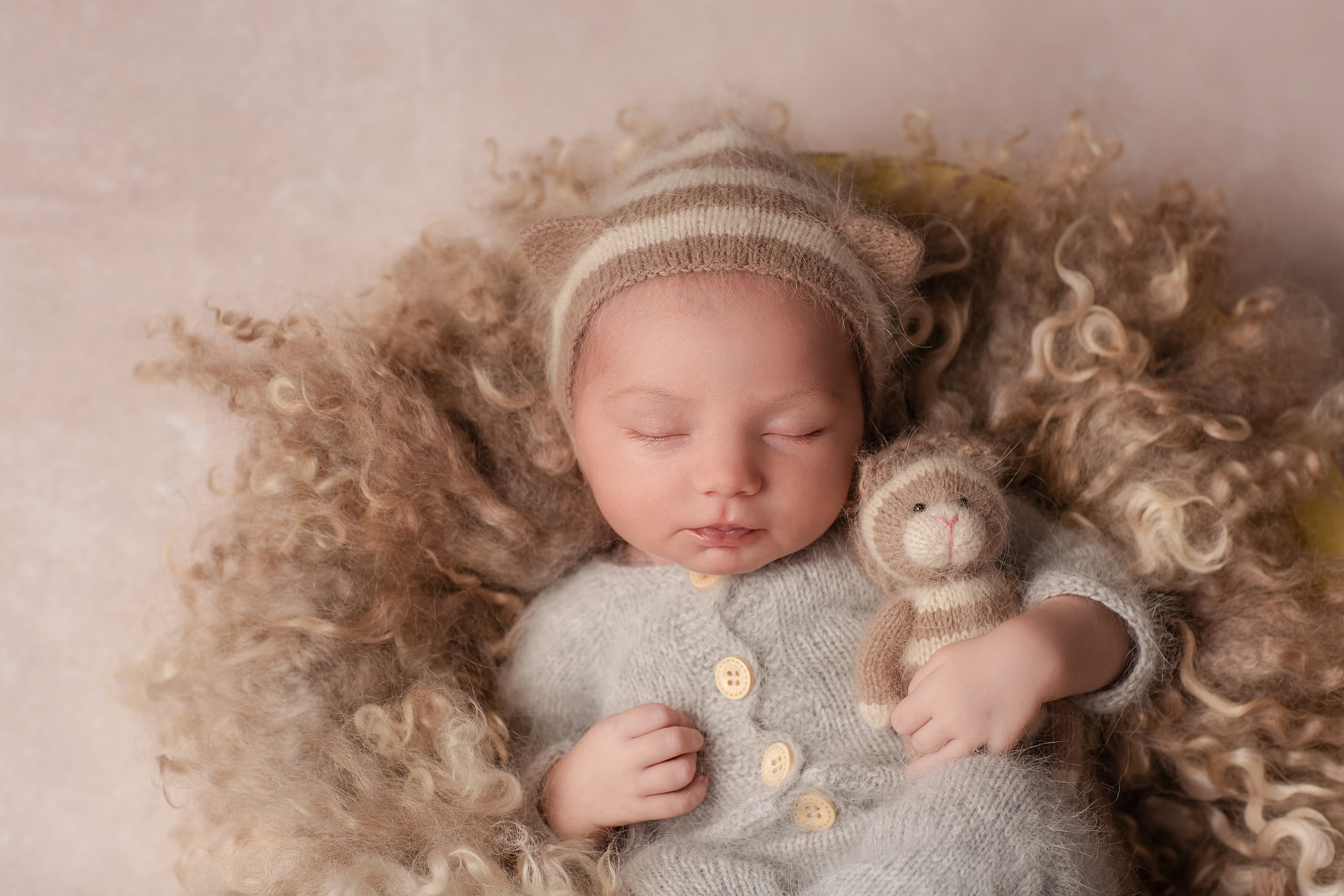 новорожденный малыш в бежевом костюме котенка с мягкой игрушкой в руках