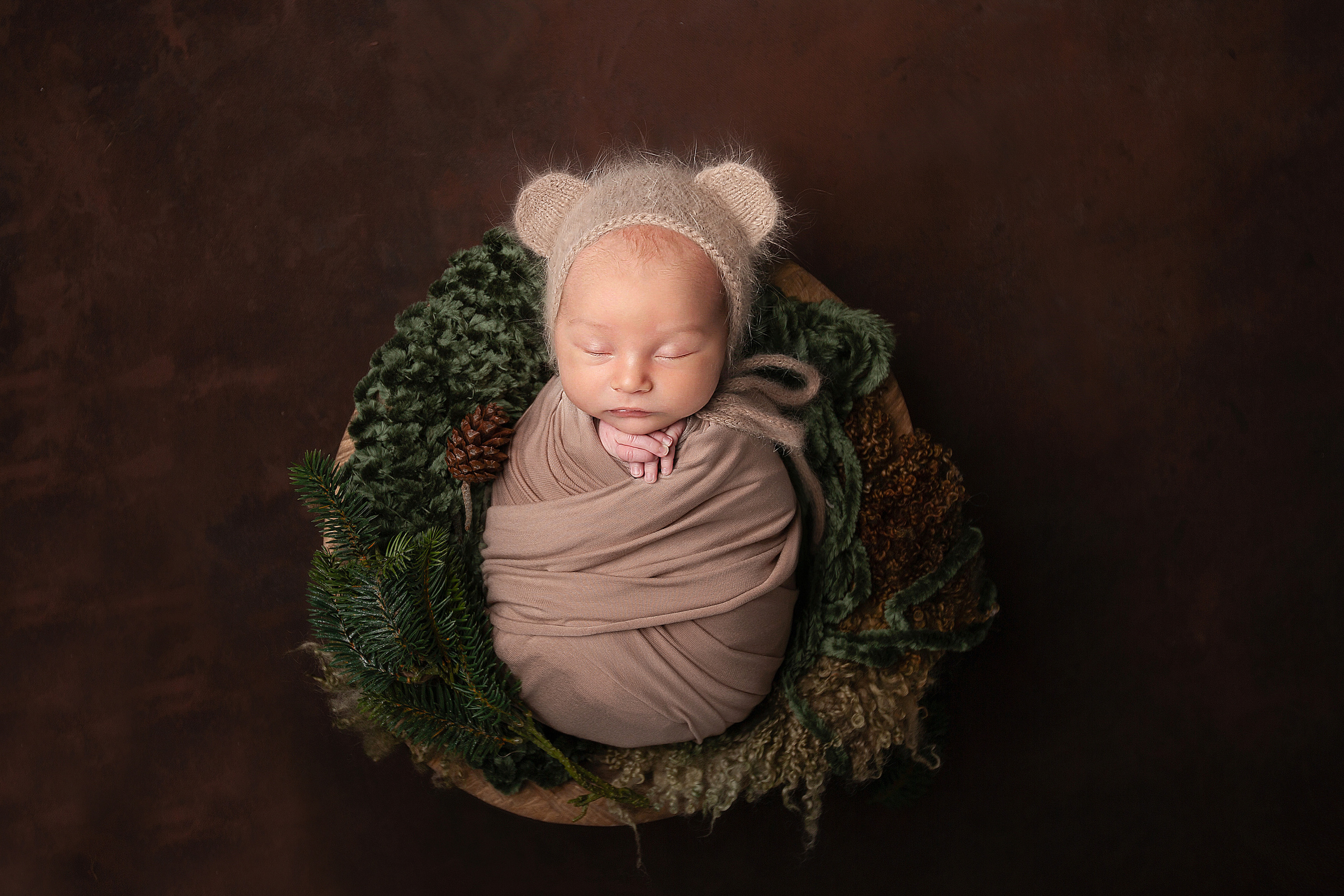 спящий новорожденный малыш в обмотке в корзине с новогодними шишками
