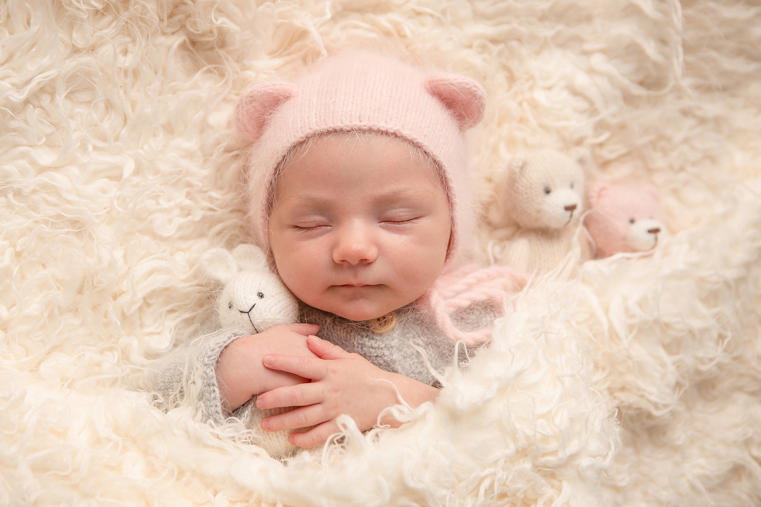 новорожденный малыш в шапочке с ушками и мягкими игрушками в руках