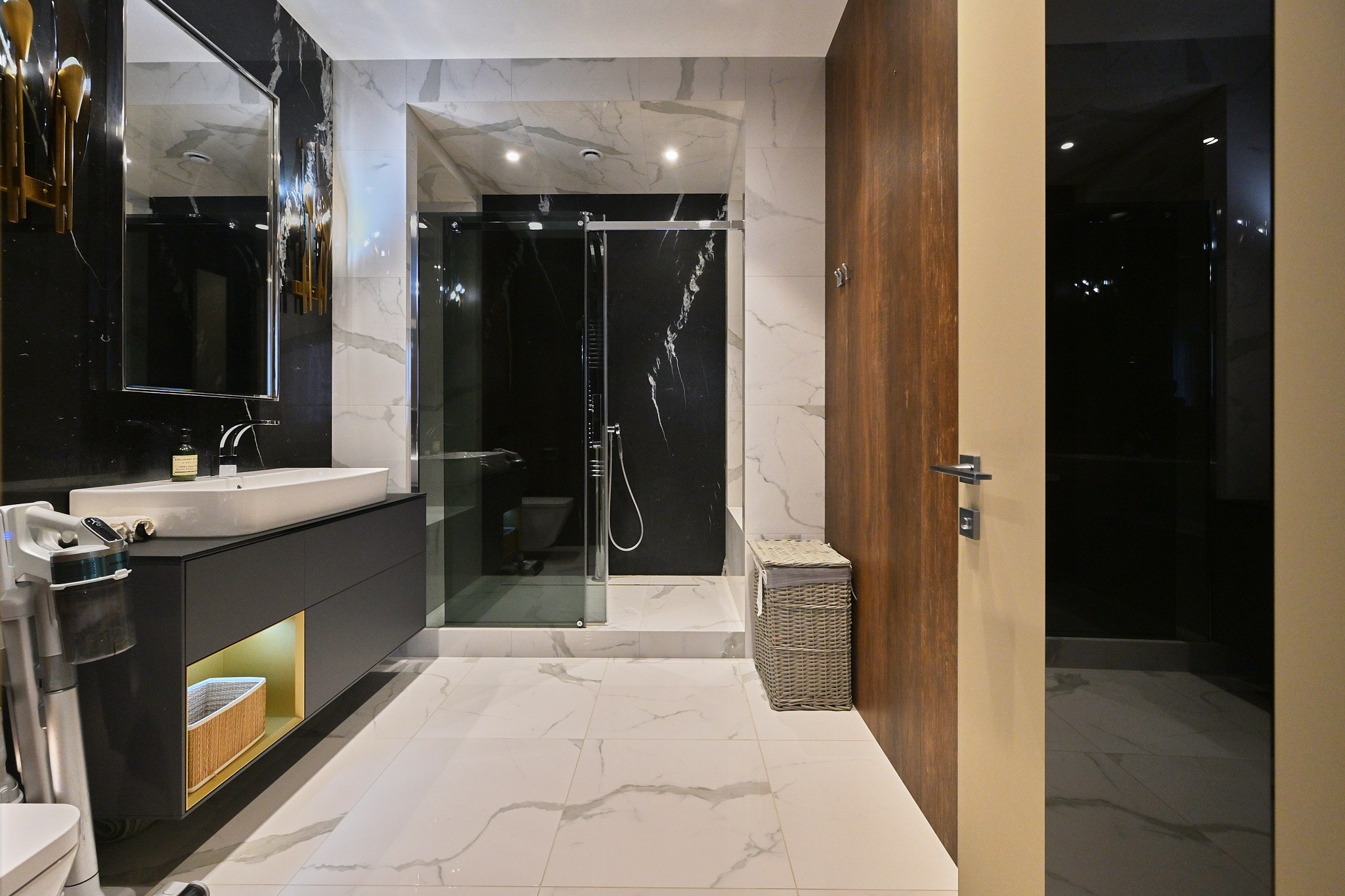 светлые плиты одна стена с темной плиткой и большим зеркалом серые тумбы белая раковина душевая кабина бежевая дверь 