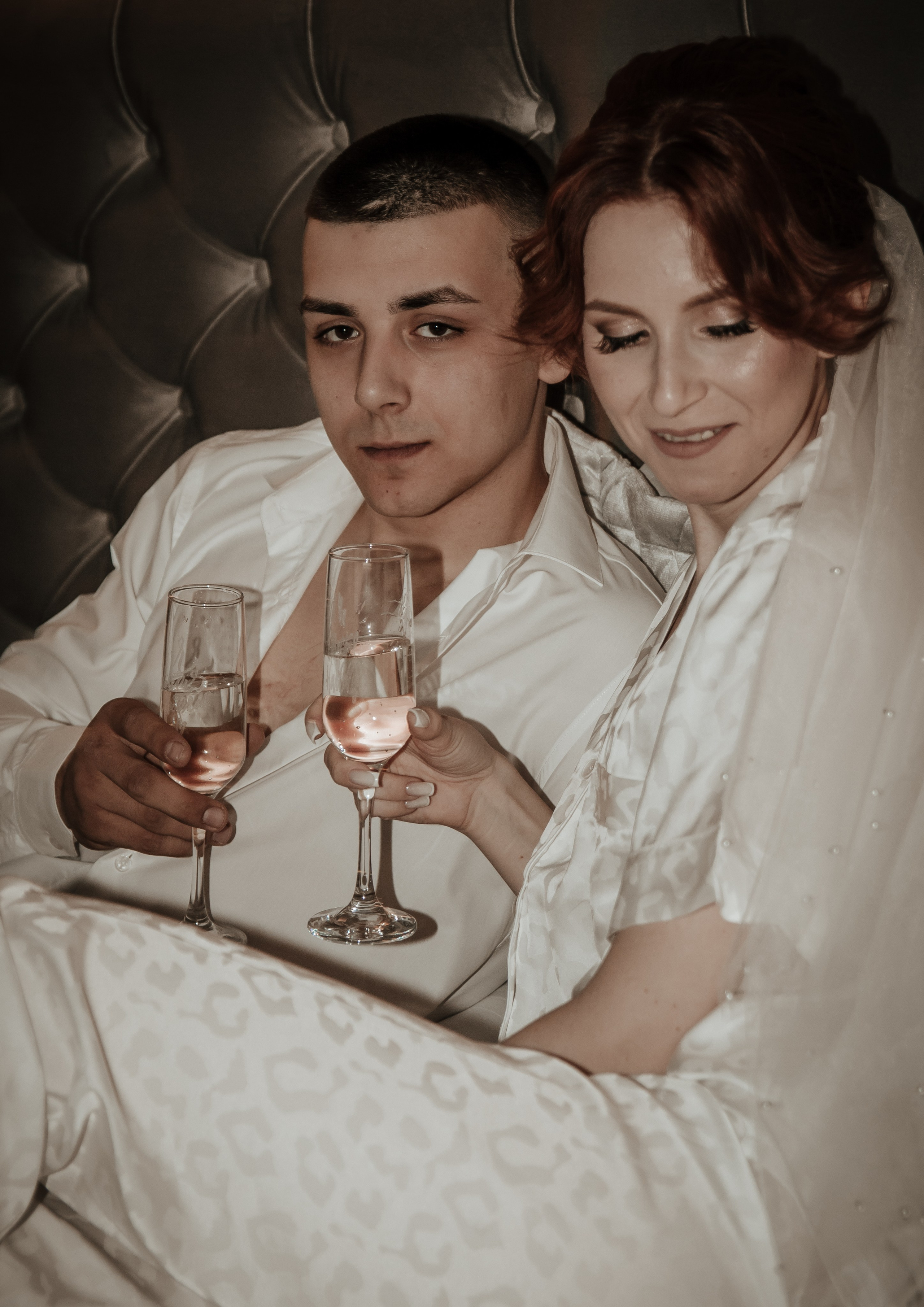 молодая  пара красиво позирует на кровати с бокалом шампанского