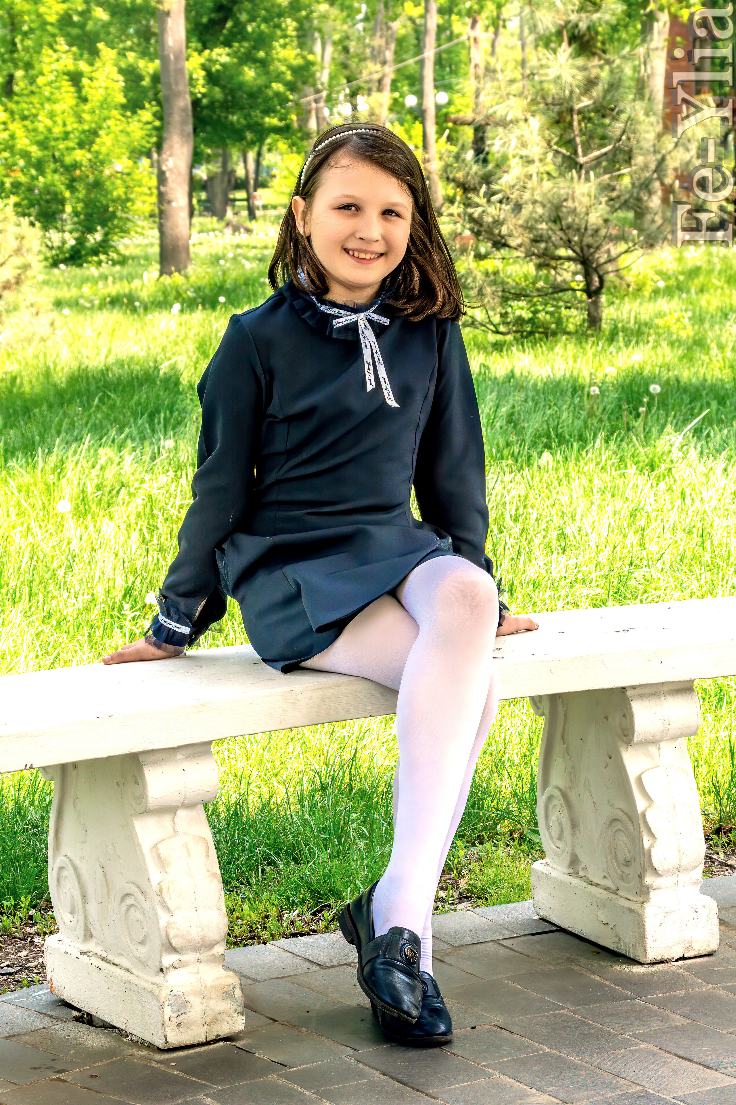 девочка в школьной форме сидит на лавочке в парке и улыбается