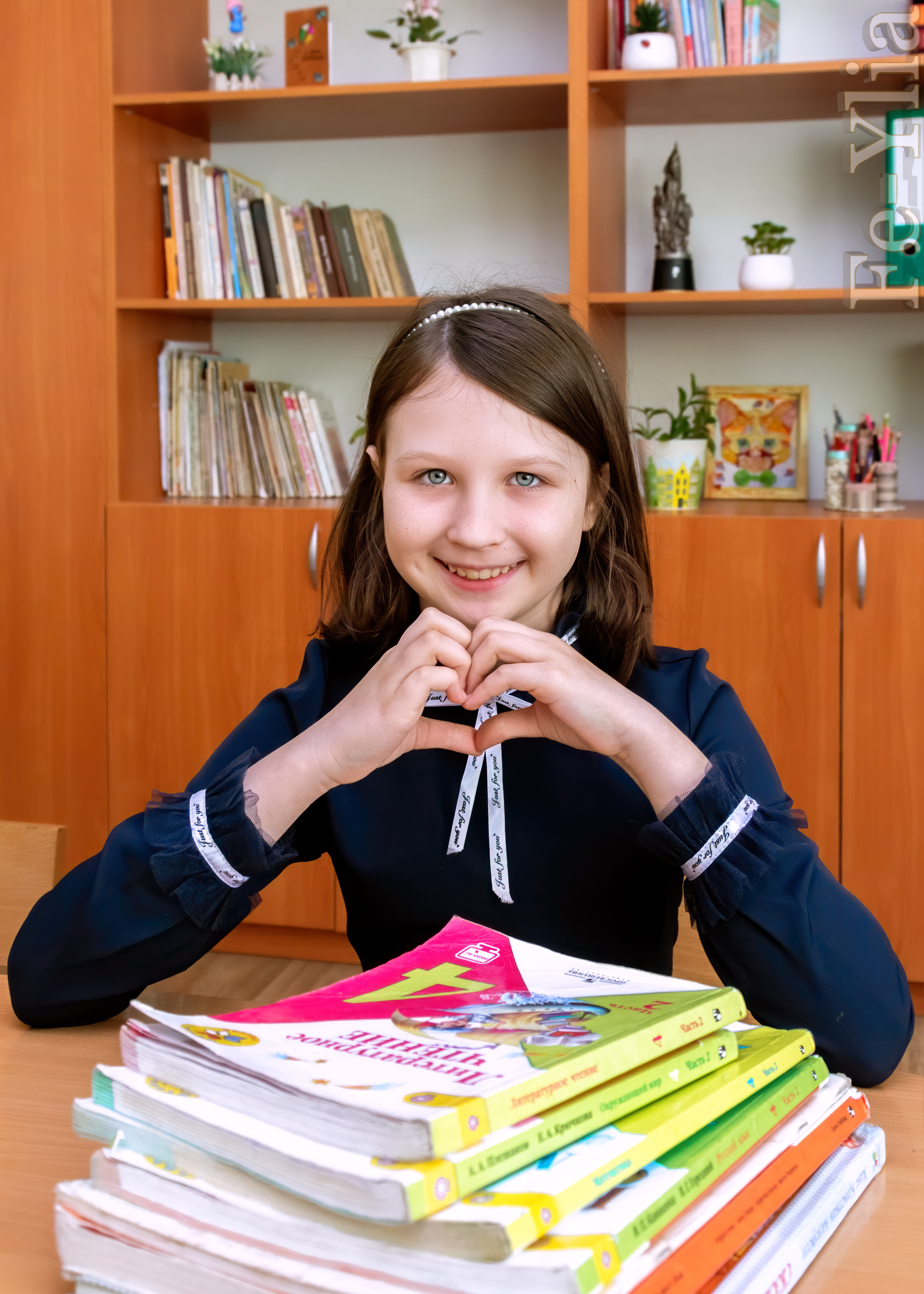 Девочка в школьном классе  за партой сложила руки сердечком