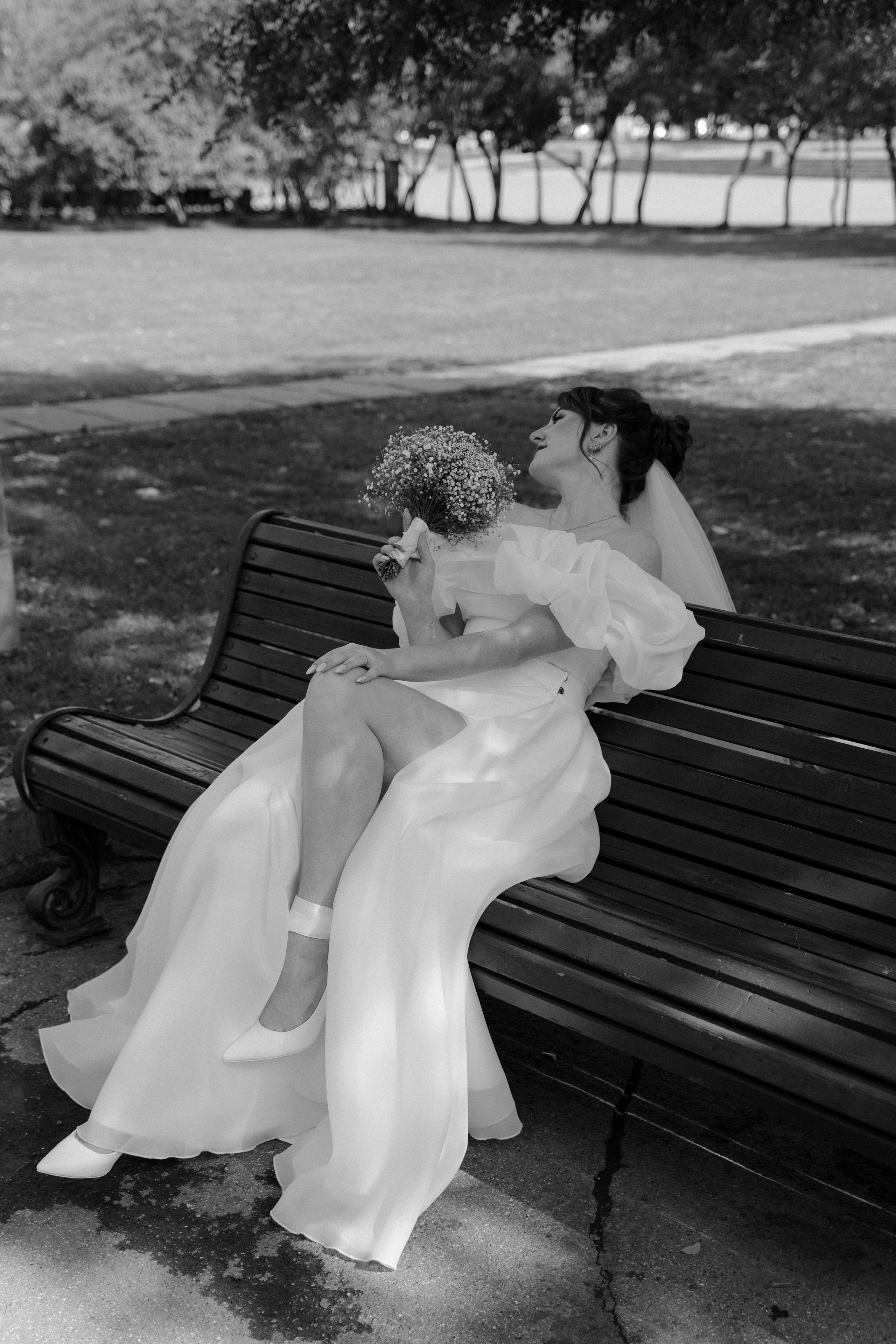 Невеста сидит на скамейке в парке с букетом 