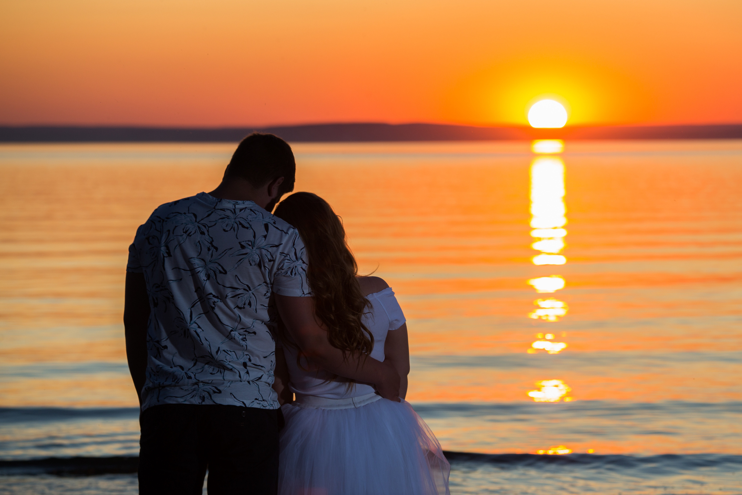 мужчина и женщина стоят и смотрят на закатное солнце у воды