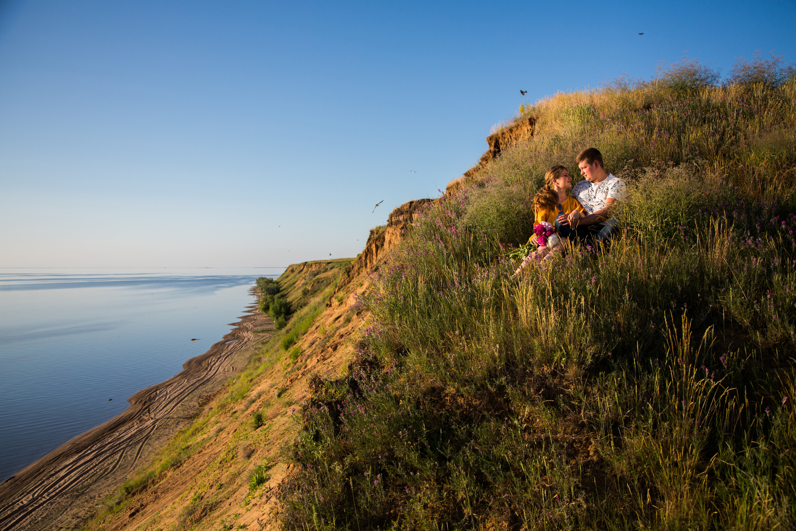 молодая пара сидит на склоне горы перед морем