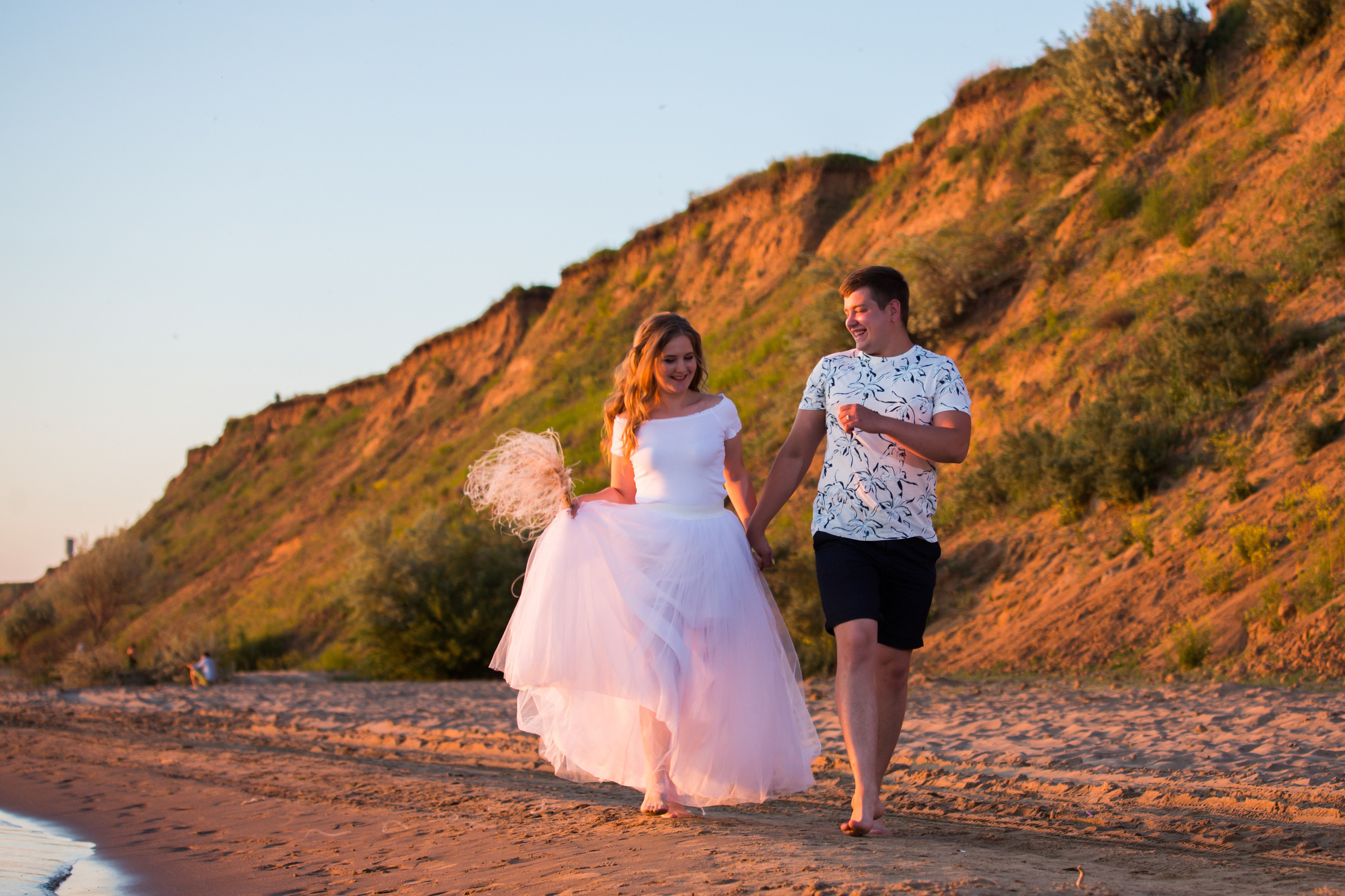 юноша и девушка у подножья горы весело бегут взявшись за руки