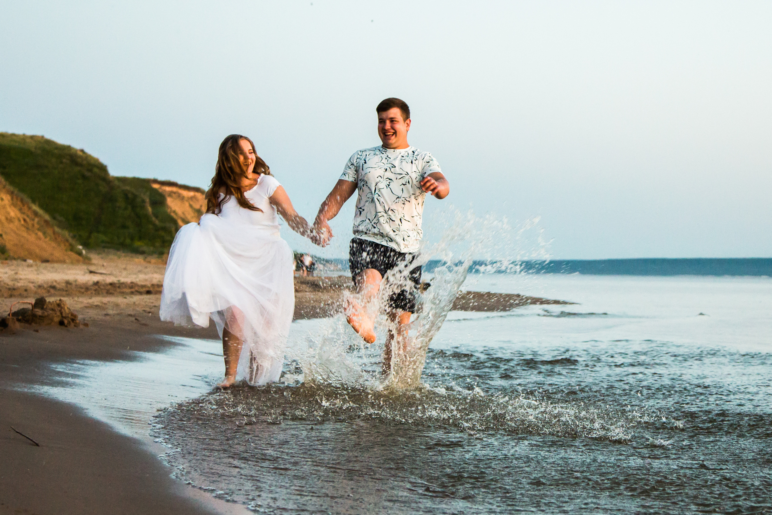 девушка и парень бегут веселясь по краю берега, устраивая брызги