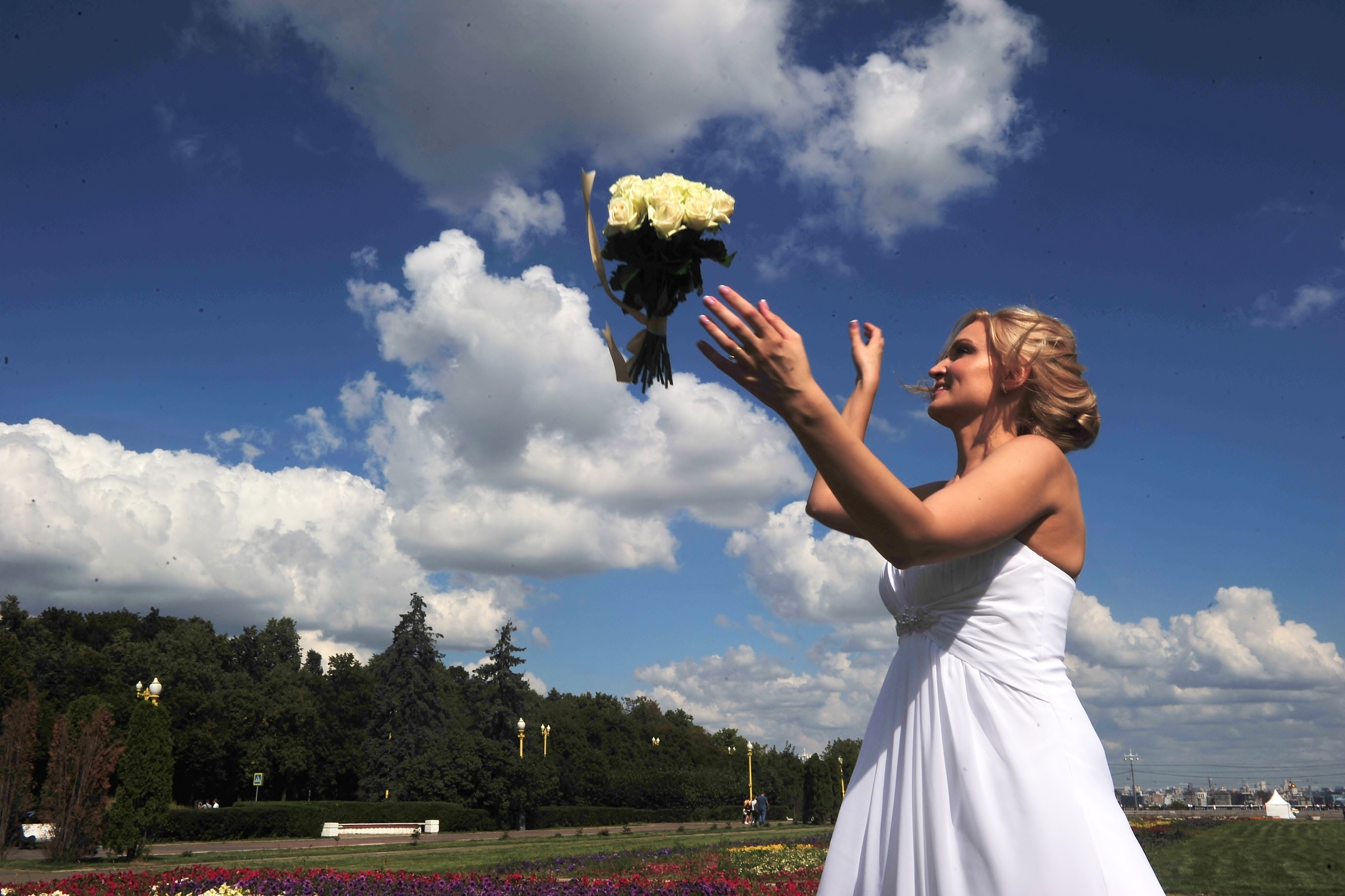 Свадьба на Воробьёвых Горах рядом с МГУ, невеста кидает свадебный букет на фоне ярко-синего неба